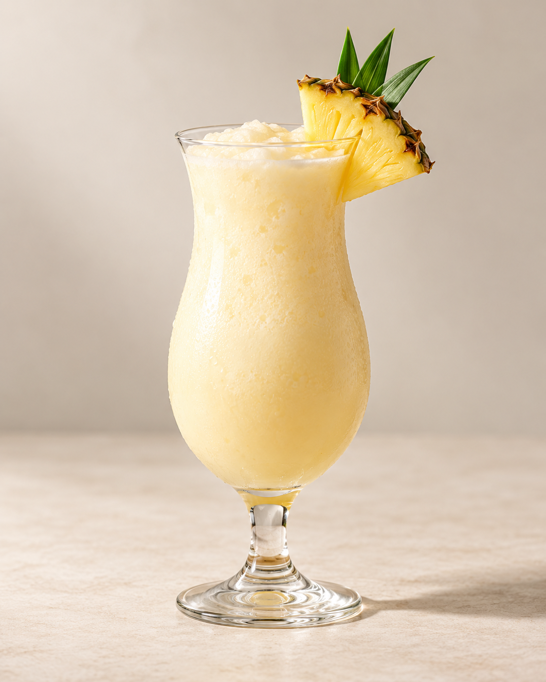 A tall glass filled with pineapple frozen drink garnished with a pineapple slice and green leaves.