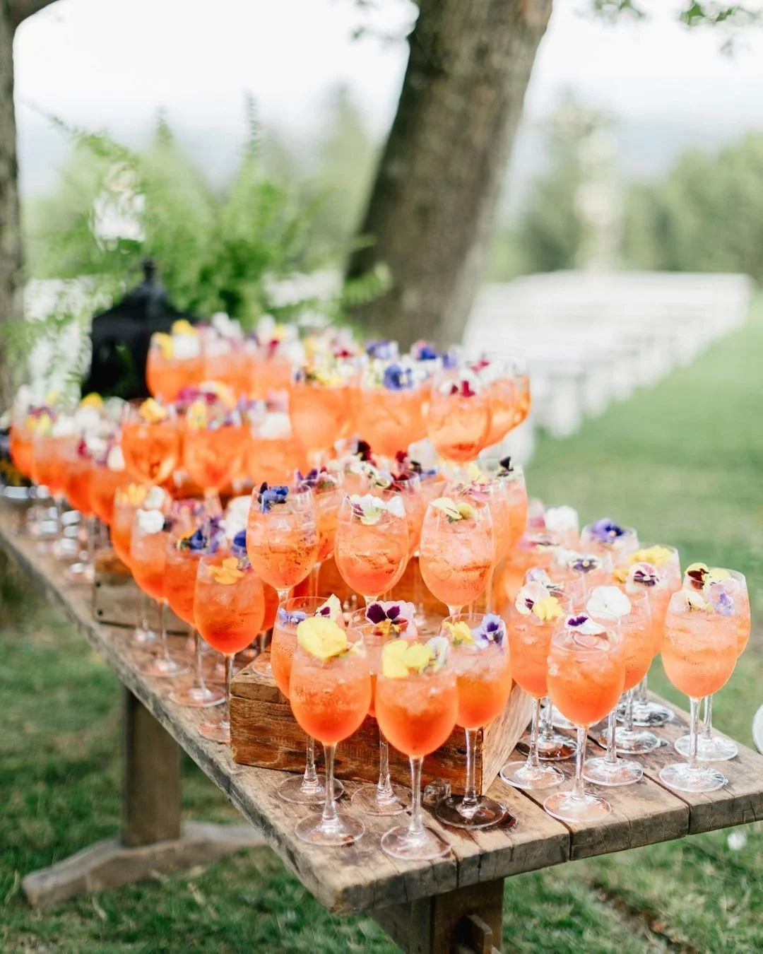 Verres de cocktail orange avec des fleurs comestibles sur une table en bois lors d'un événement en plein air.