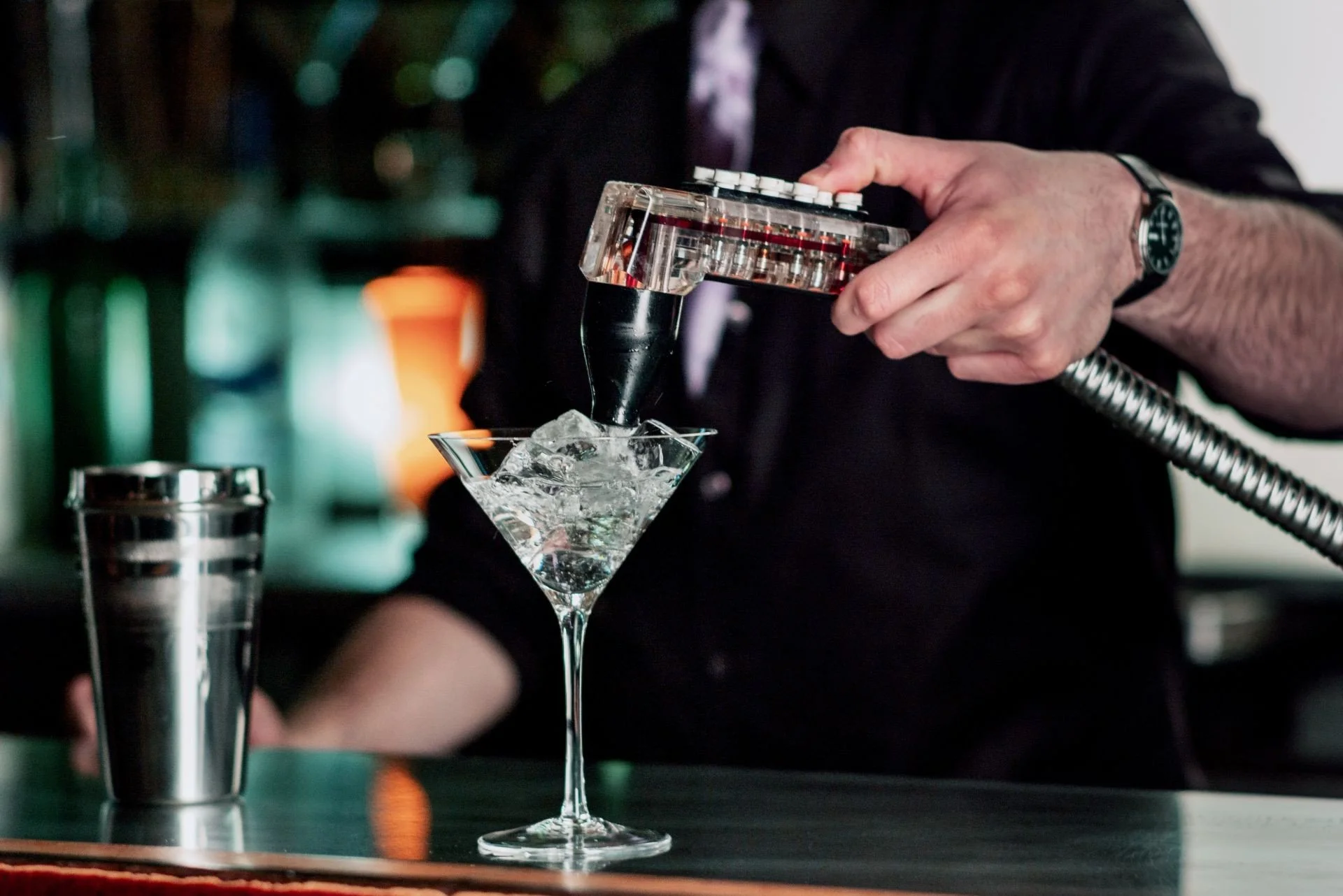 Un barman verse de la vodka dans un verre à cocktail rempli de glaçons, utilisant un appareil à diffusion de la vodka.