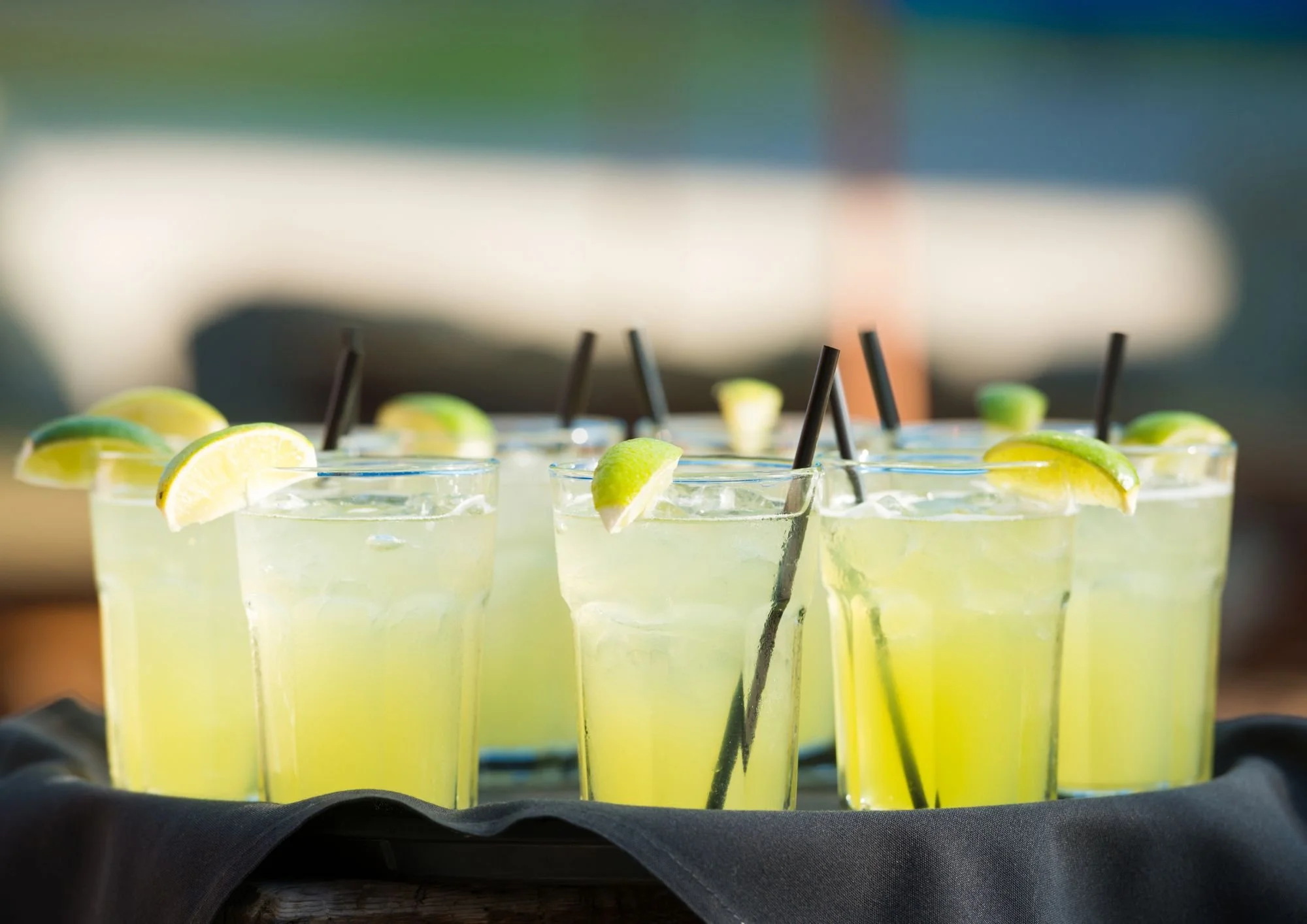 Verres de margarita citronnée garnis de quartiers de citron et de lime, avec des pailles noires, posés sur une surface sombre.