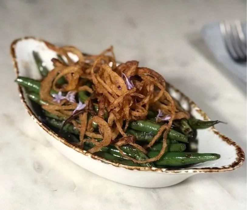 Green beans topped with crispy fried onions on a white dish.