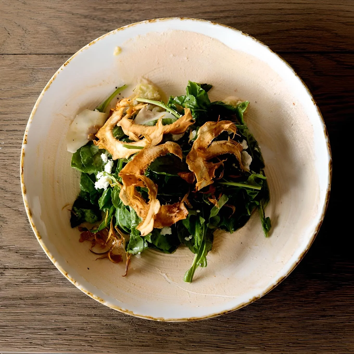 A bowl of mixed greens salad topped with dried mushroom slices, on a wooden table
