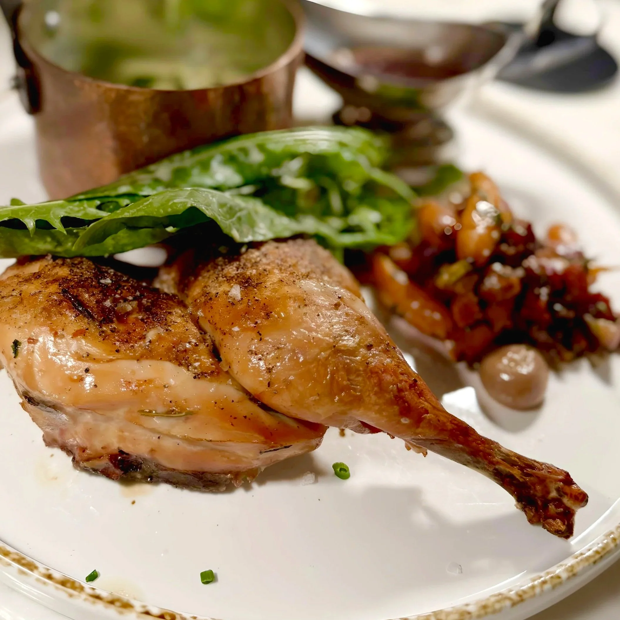 Close-up of a cooked chicken thigh on a white plate with green herbs.