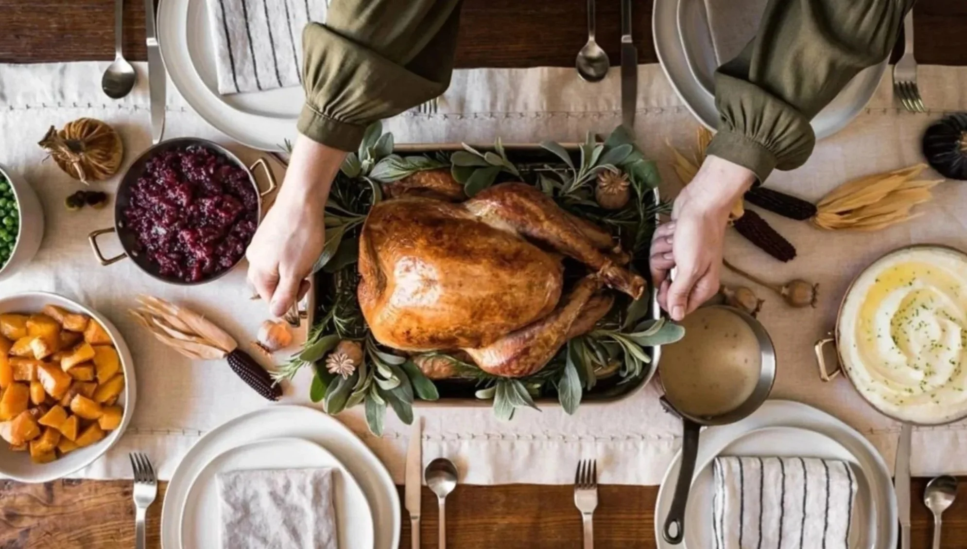Top-down view of a cooked turkey on a green leafy bed at a dining table, surrounded by various side dishes and utensils for a meal.
