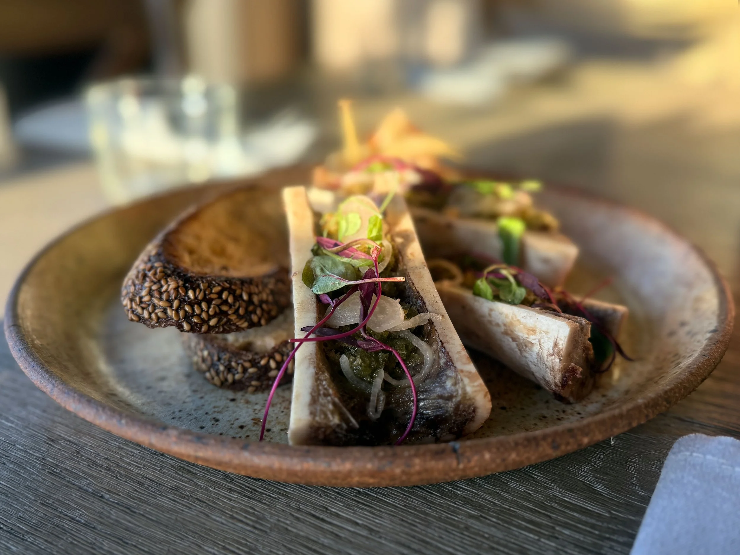 Close-up photo of sushi rolls with various toppings, including sesame seeds and microgreens, served on a ceramic plate.