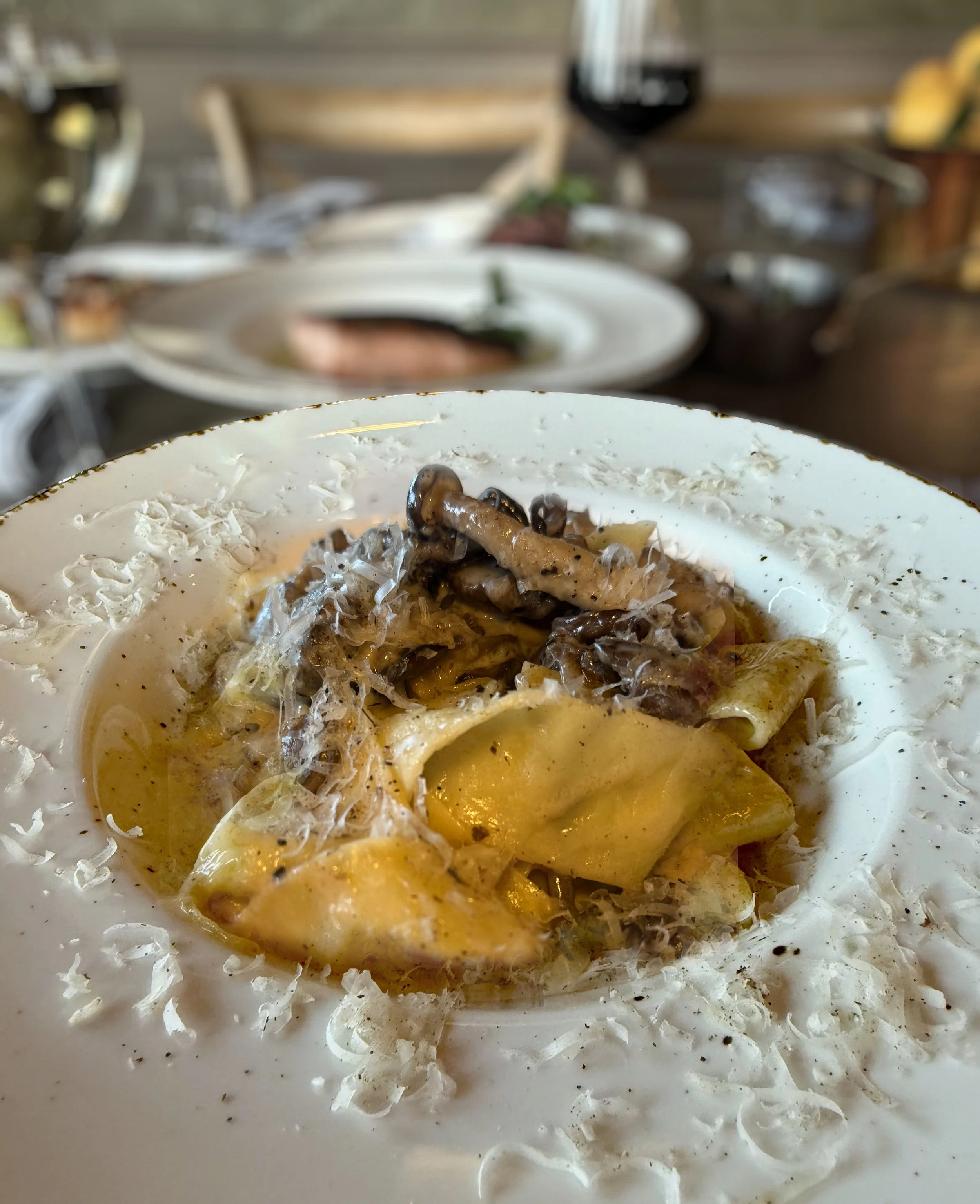 Close-up of a plate of food with creamy sauce, mushrooms, and cheese, with a blurred background of a restaurant table setting.
