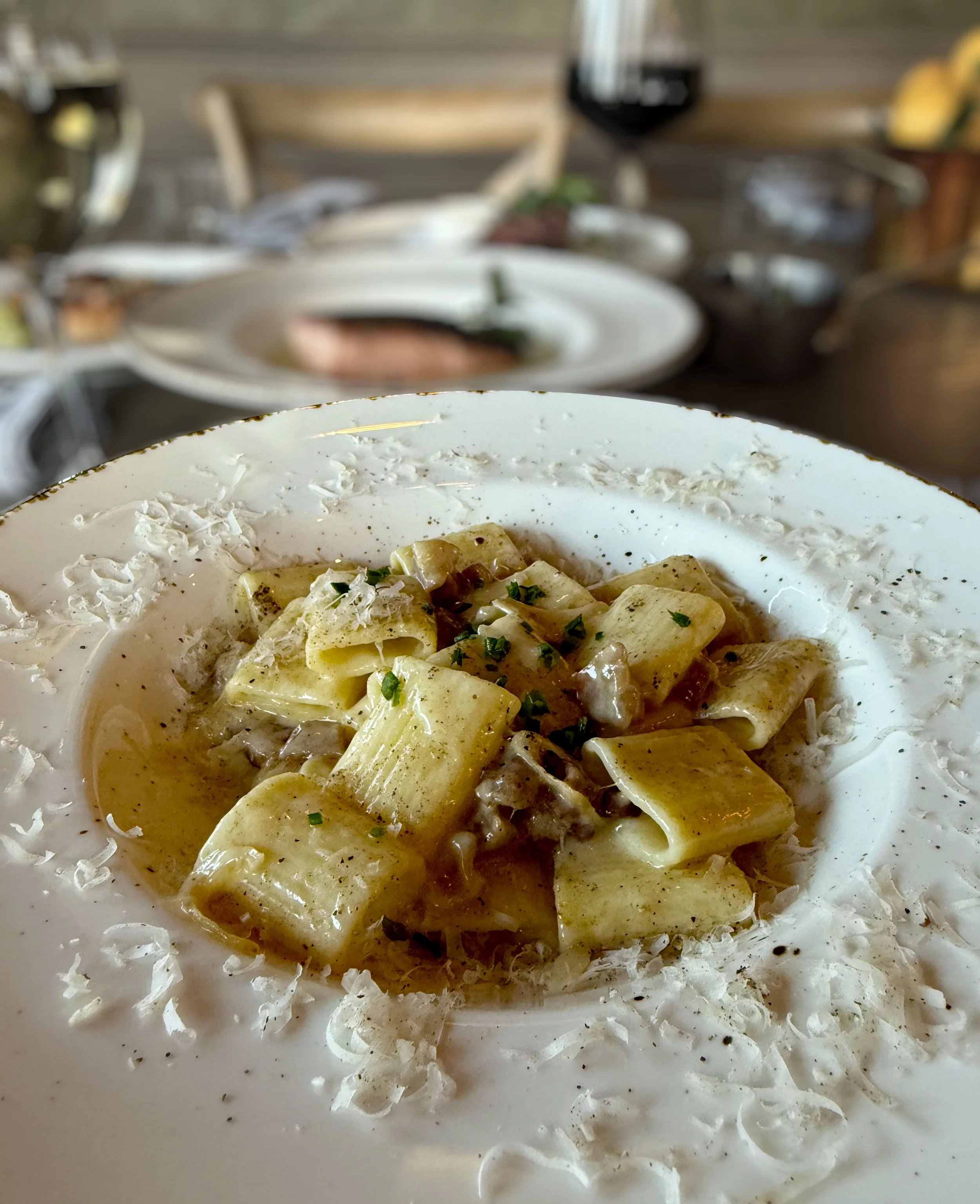 Close-up of a plate with fettuccine pasta in creamy sauce, garnished with chopped herbs, on a white plate with shredded cheese around the edge.