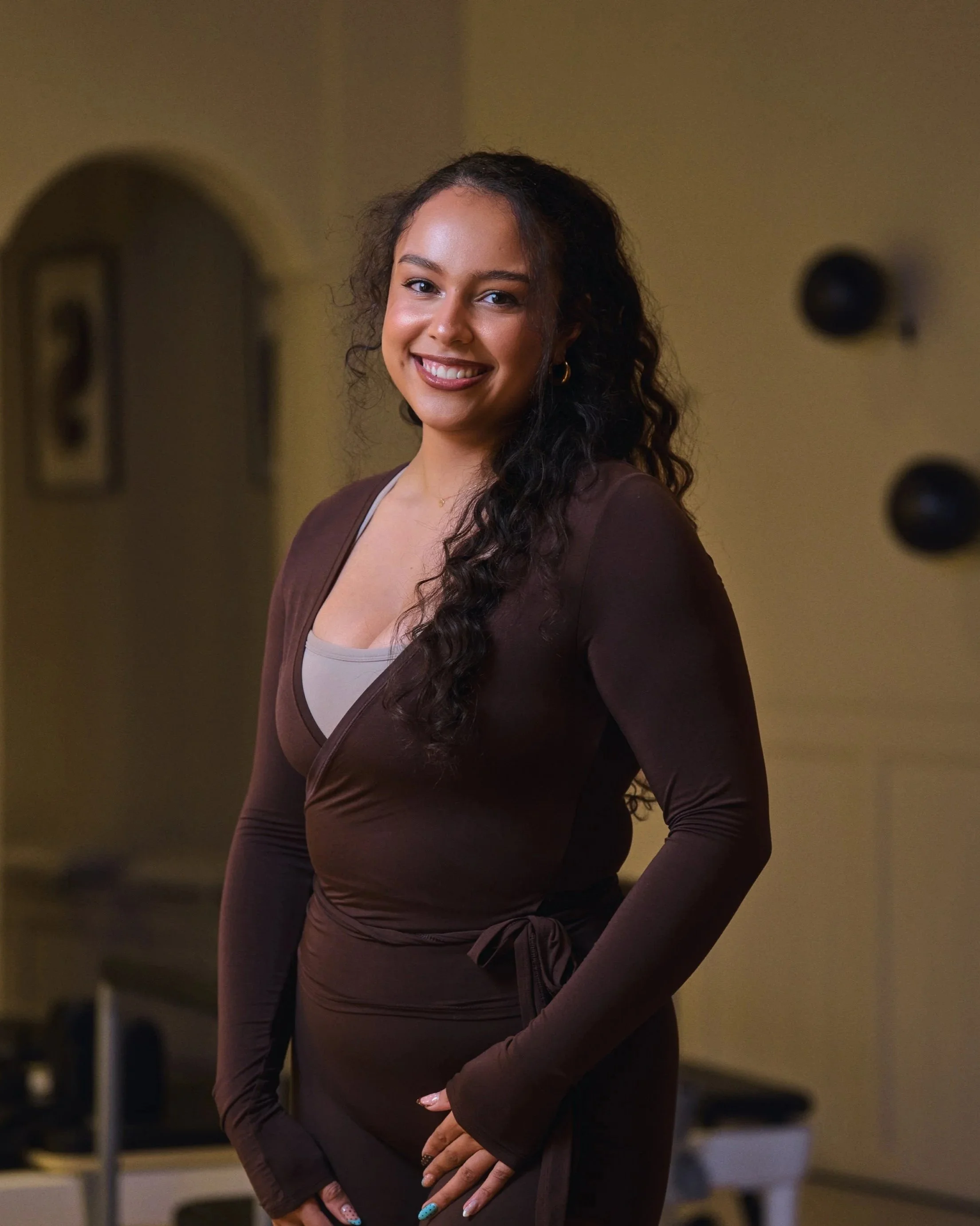 Reformer Pilates Instructrice in de reformer studio in hartje Leeuwarden, draagt een bruine set sportkleding, lachend