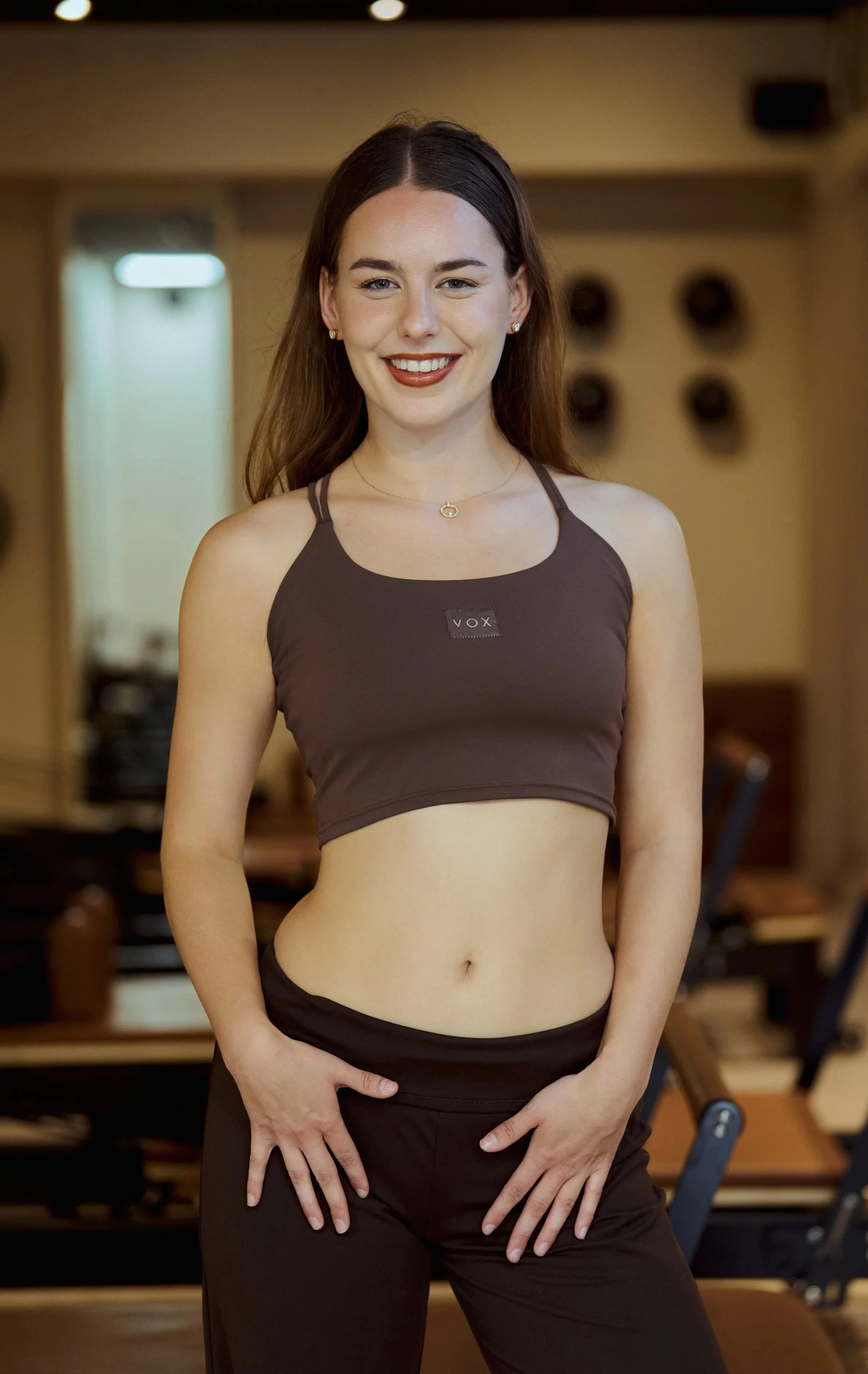 Pilates docente bij Pilates Avenue poseert zelfverzekerd in een bruine sportoutfit, in de luxe Groningse studio.