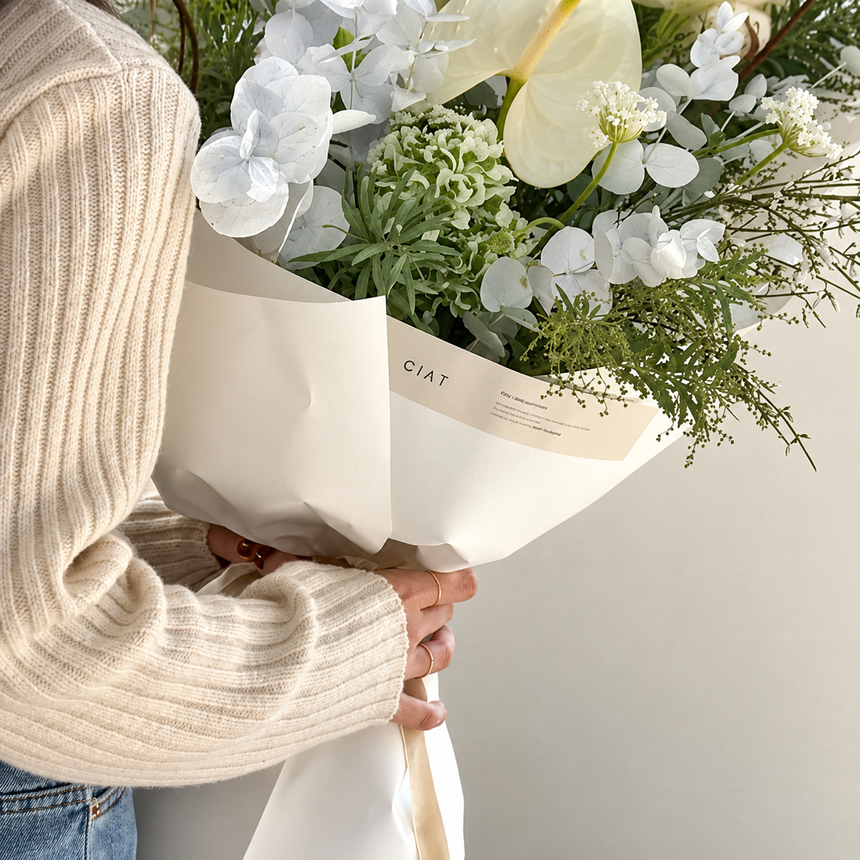Person holding a bouquet of white flowers wrapped in white paper.