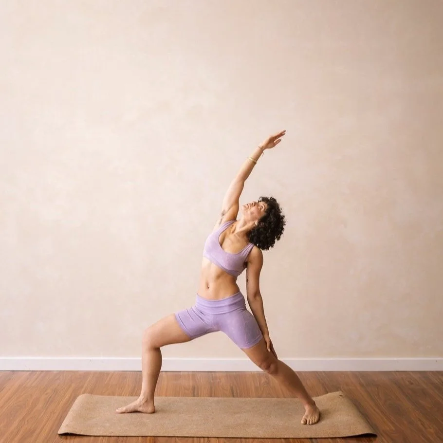 Person practicing yoga in reverse warrior pose on a mat, wearing purple workout clothes, in a minimalist room.