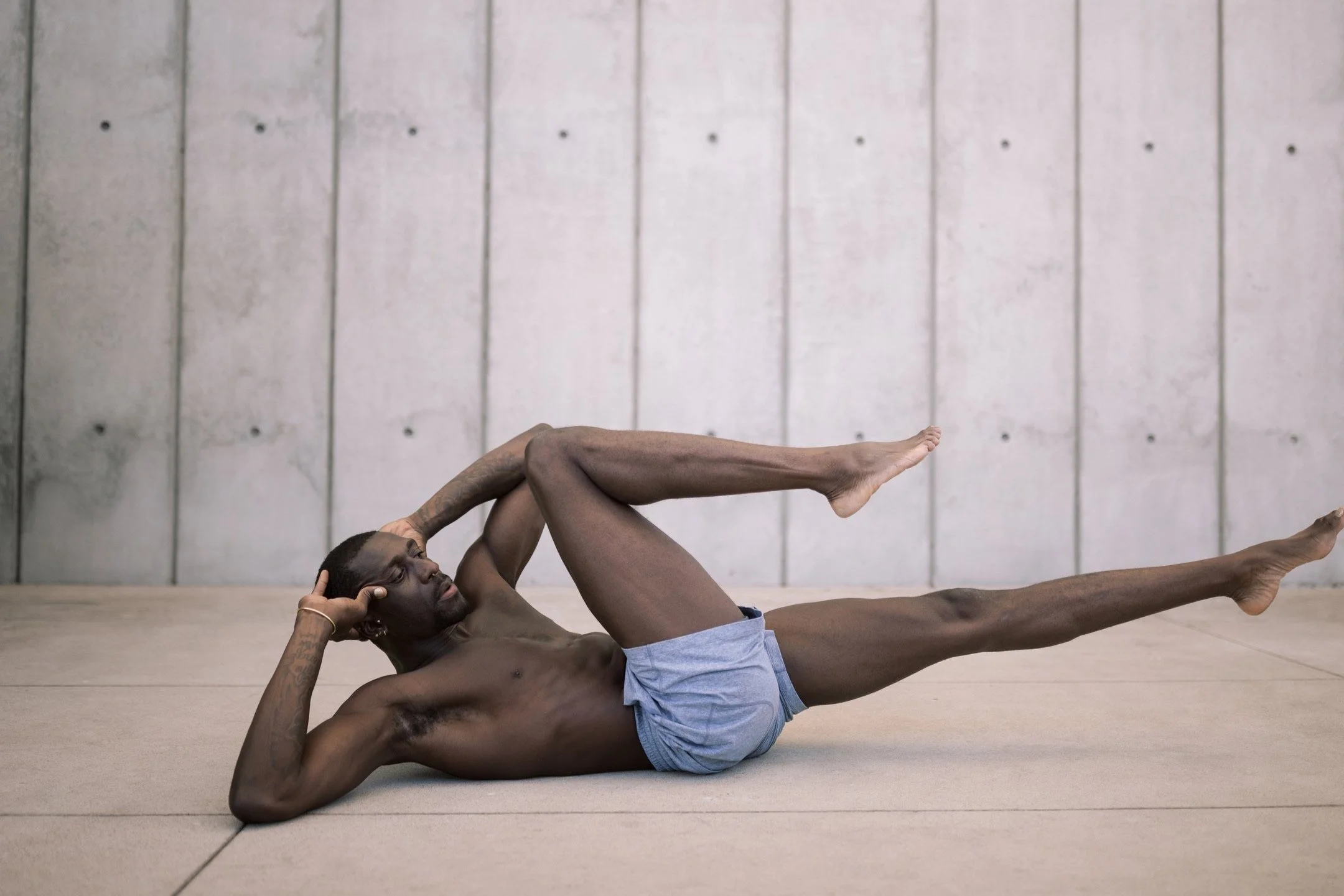 Man performing bicycle crunch exercise against a concrete wall background.