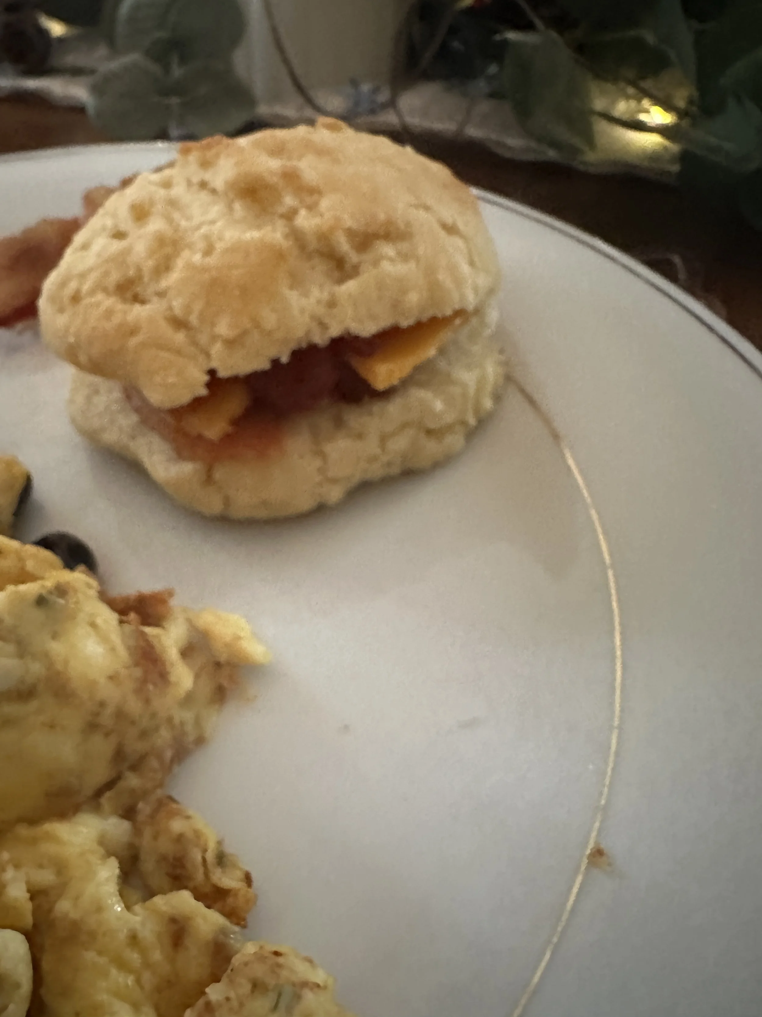 A biscuit sandwich with bacon and cheese on a white plate.