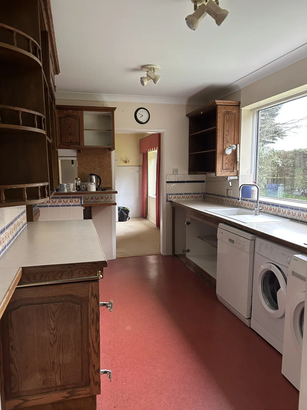 The same Thakeham kitchen before the work, a narrow galley with dark units and a red floor