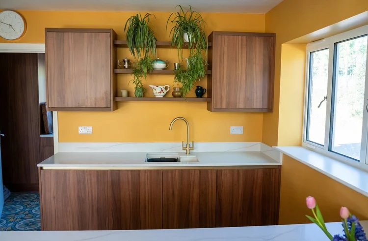Walnut sink run with open shelves against a yellow wall, Storrington