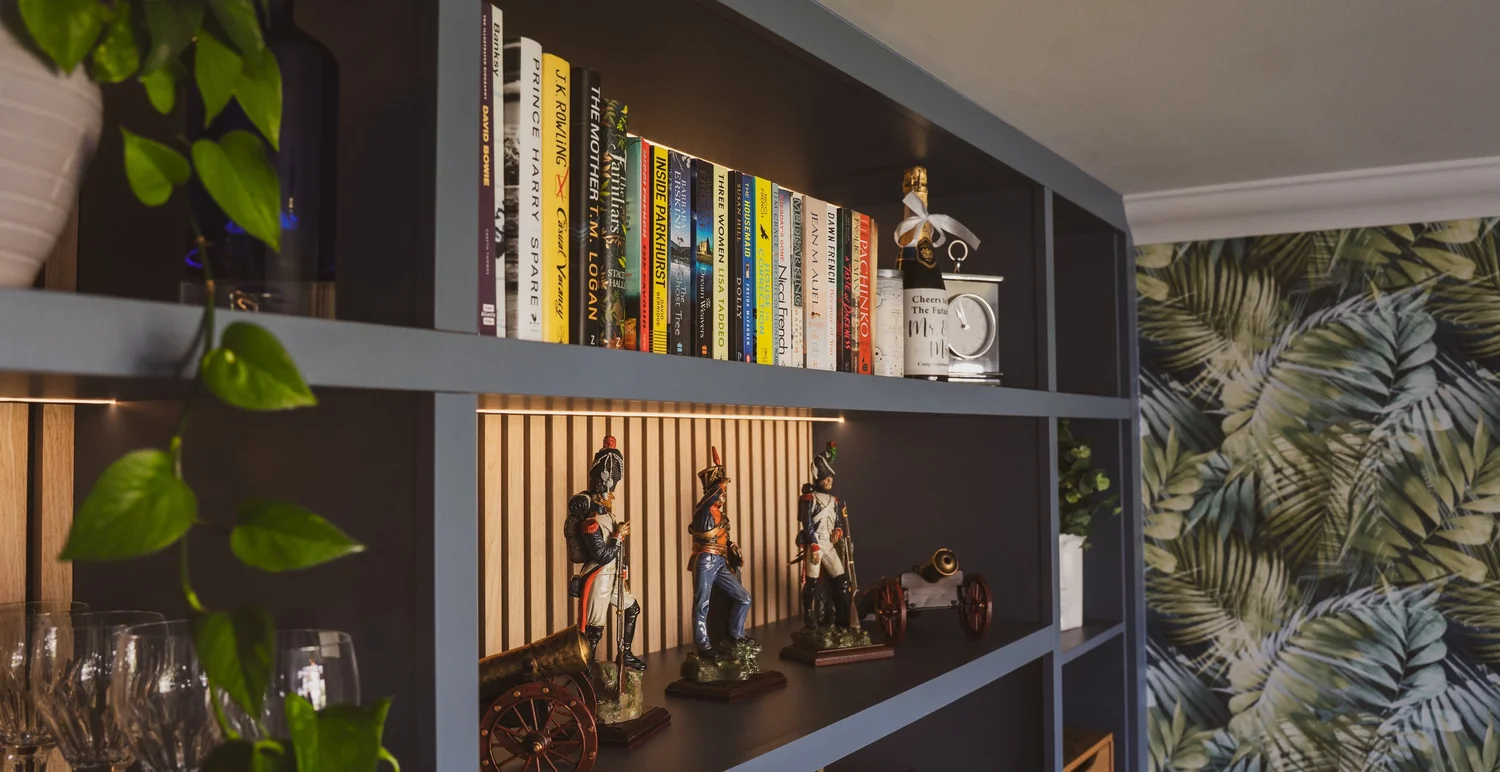 Open shelves lit from below against vertical oak panelling on a misty blue unit, Lancing