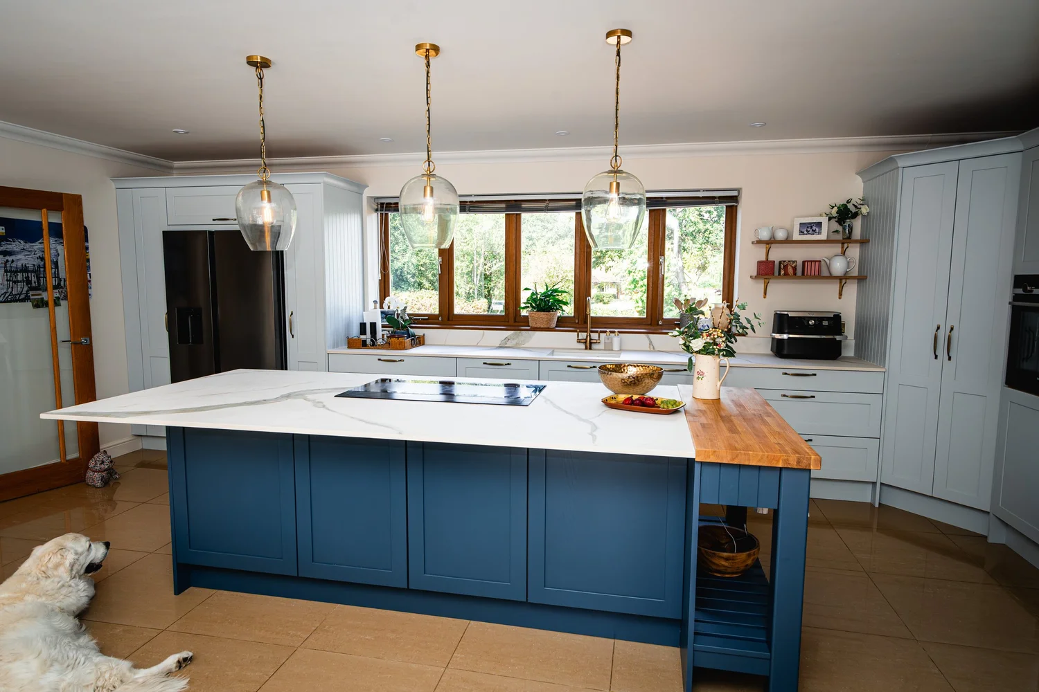 Navy island under three pendant lights in an open soft blue kitchen, West Chiltington