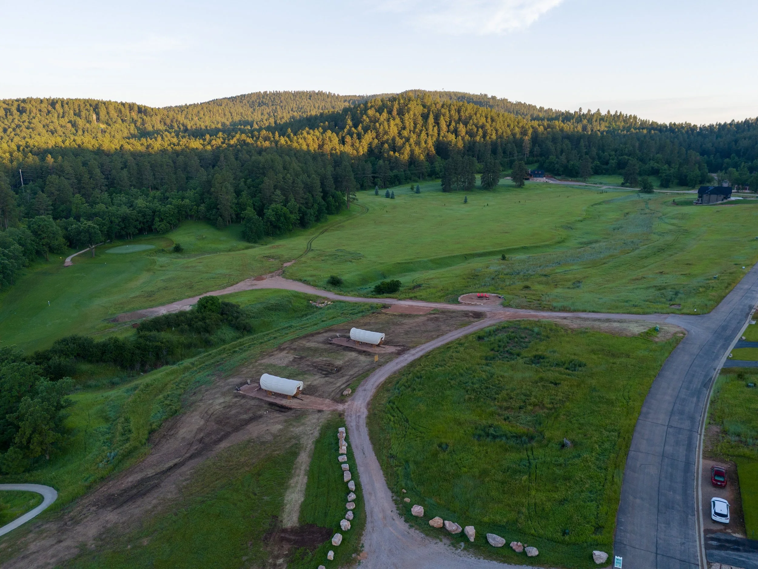 Aerial view of a developing neighborhood with cleared plots, new roads, and a golf course surrounded by forested hills.