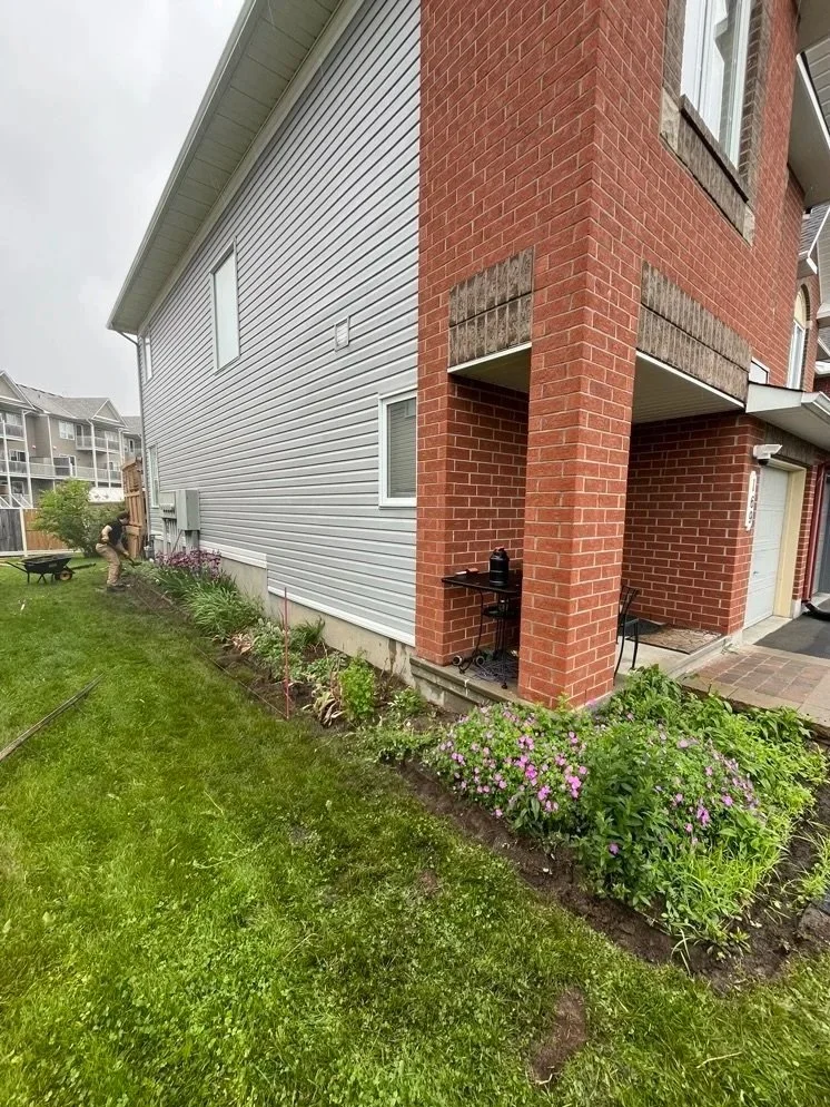 Backyard with flower bed, green grass, and a man gardening near a fence