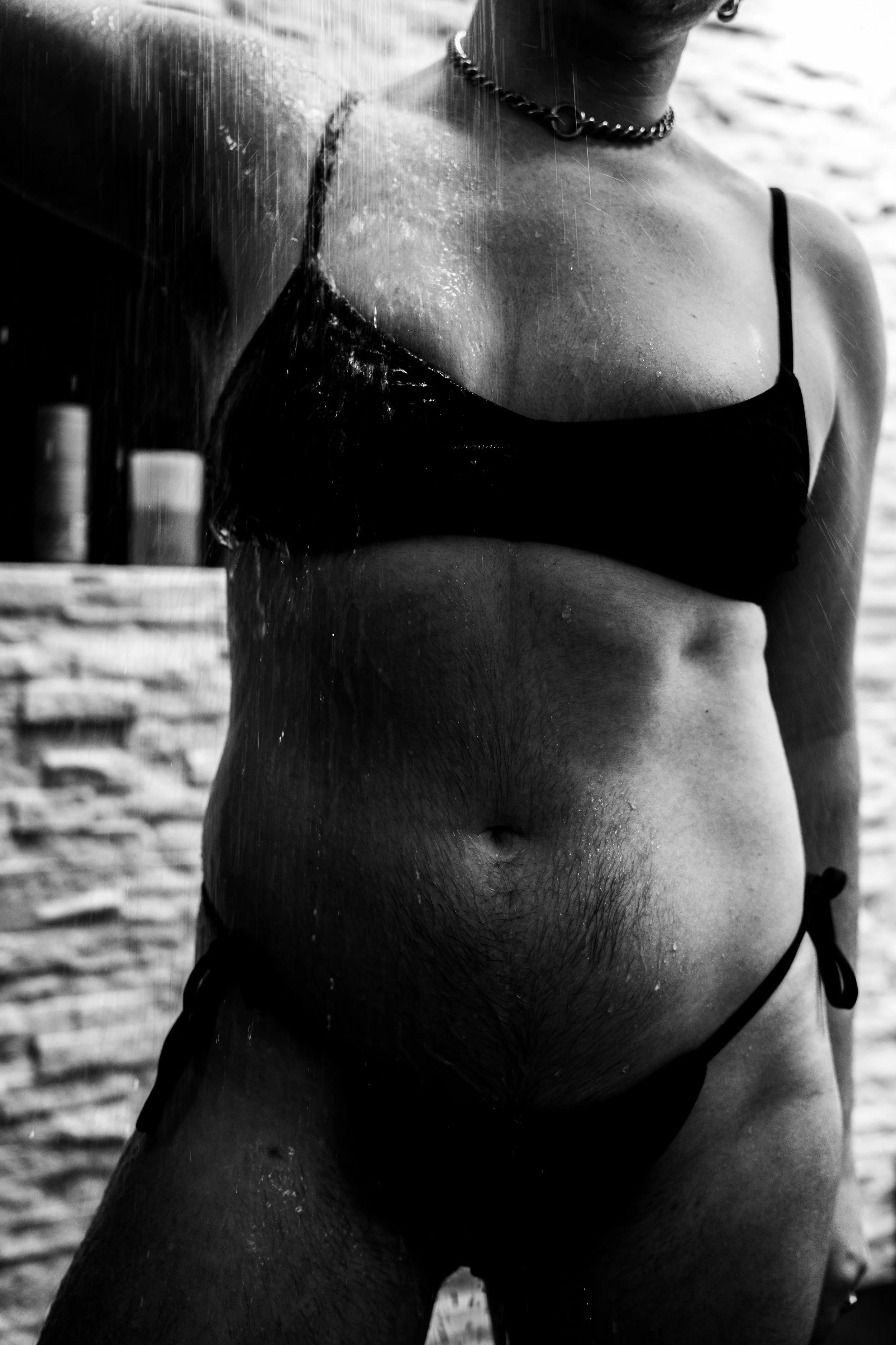 A black and white photo of a woman in a bikini top with water pouring down her body at the beach.