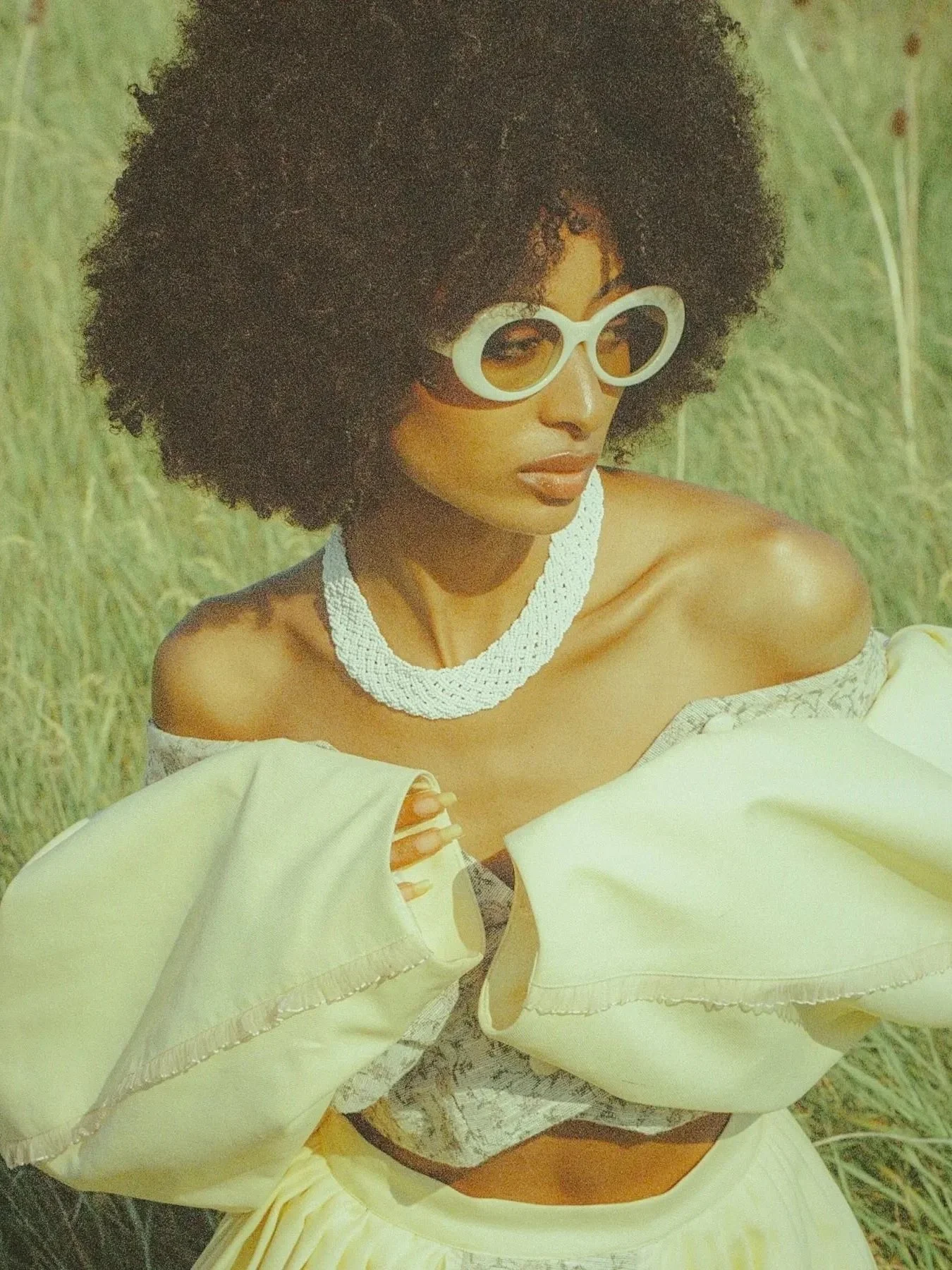 A woman with dark skin and curly hair wearing dorian who toronto fashion montreal los angeles toronto makeup artist commercial clean natural professional headshots editorial outdoor shoot nature green off the shoulders afro hair 70s inspired