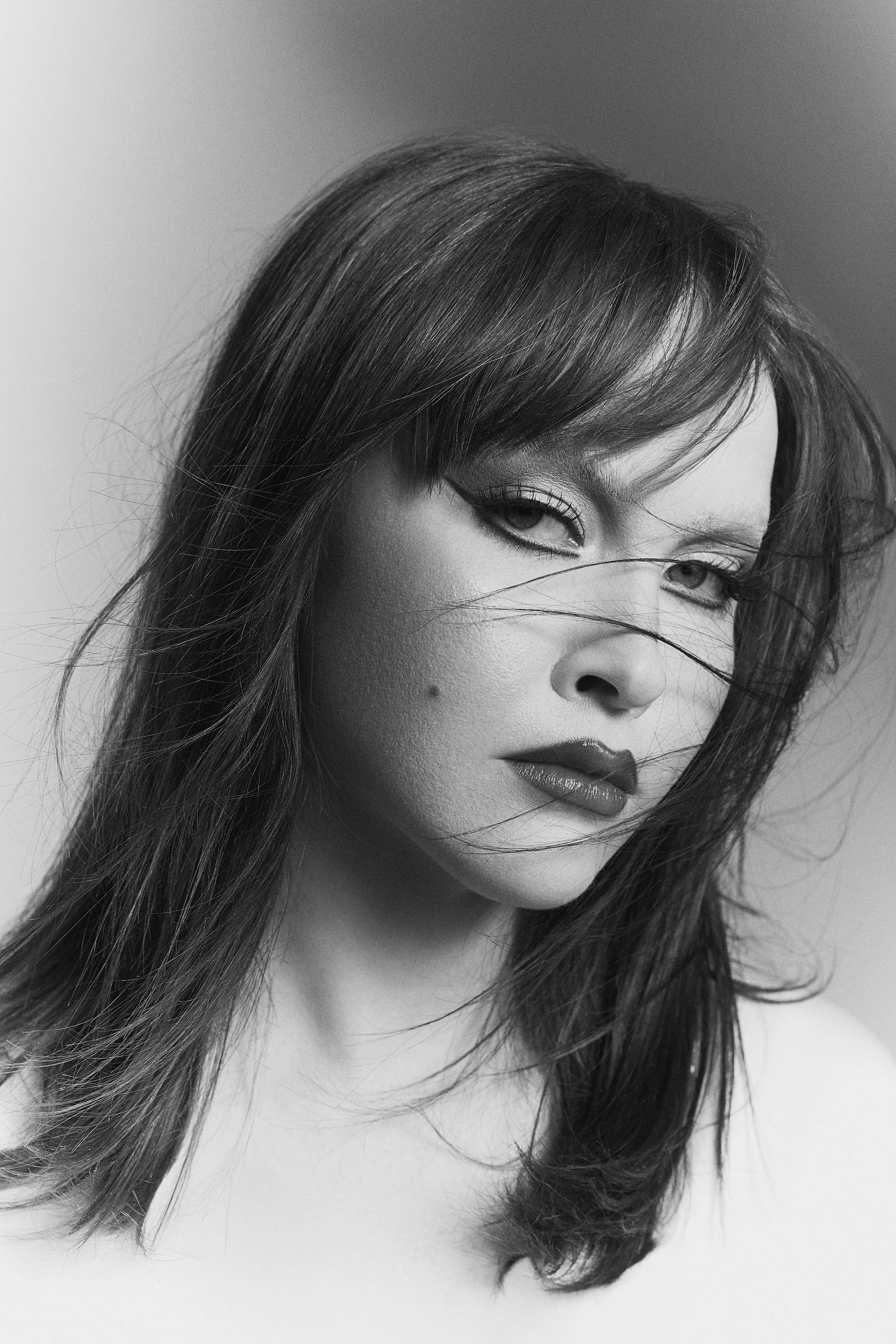 Black and white portrait of a woman with dark hair, makeup, and an intense expression.