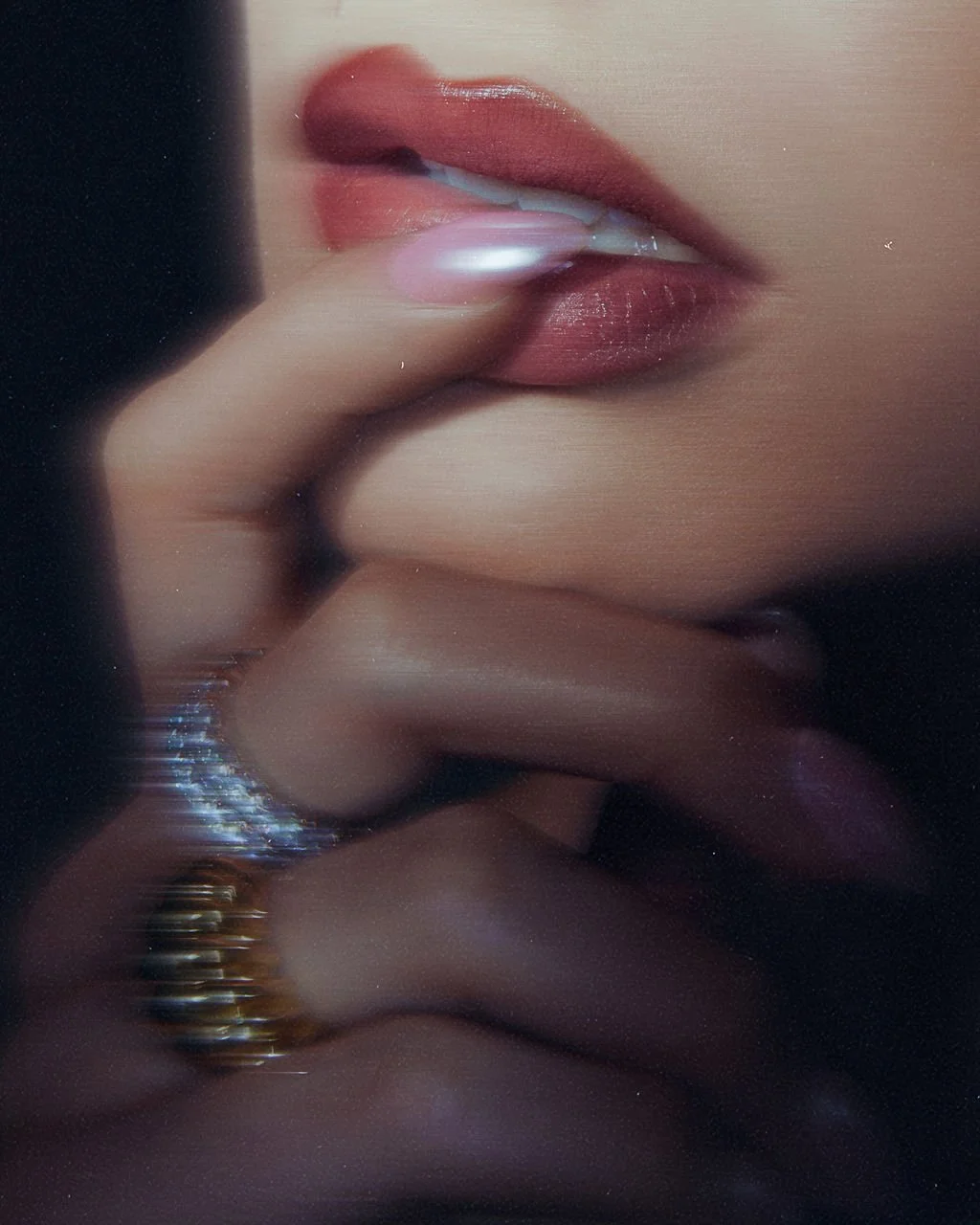 Close-up of a woman's lips with the finger resting on her lips, wearing rings, and with the reflection of her fingers visible below.