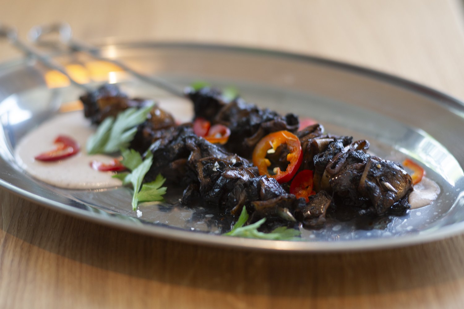 Skewers of grilled meat with red and green chili slices and garnished with fresh herbs on a silver platter.
