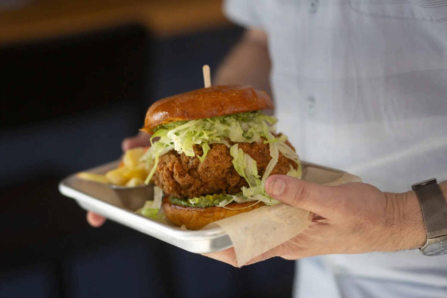 Person holding tray with fried chicken sandwich, lettuce, pickles, and sauce