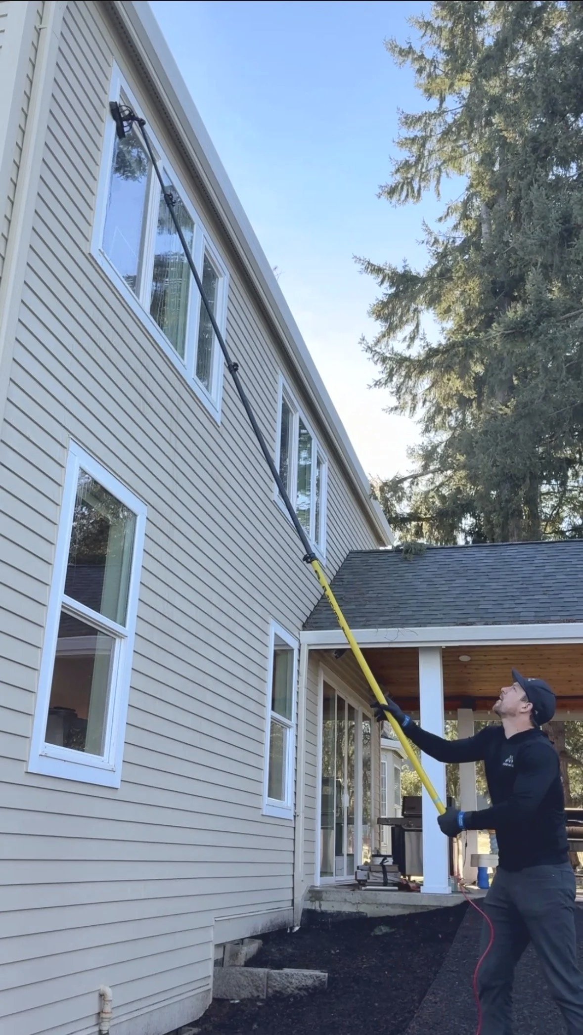 A person using a long pole to clean or wash the exterior of a house's second-story window.