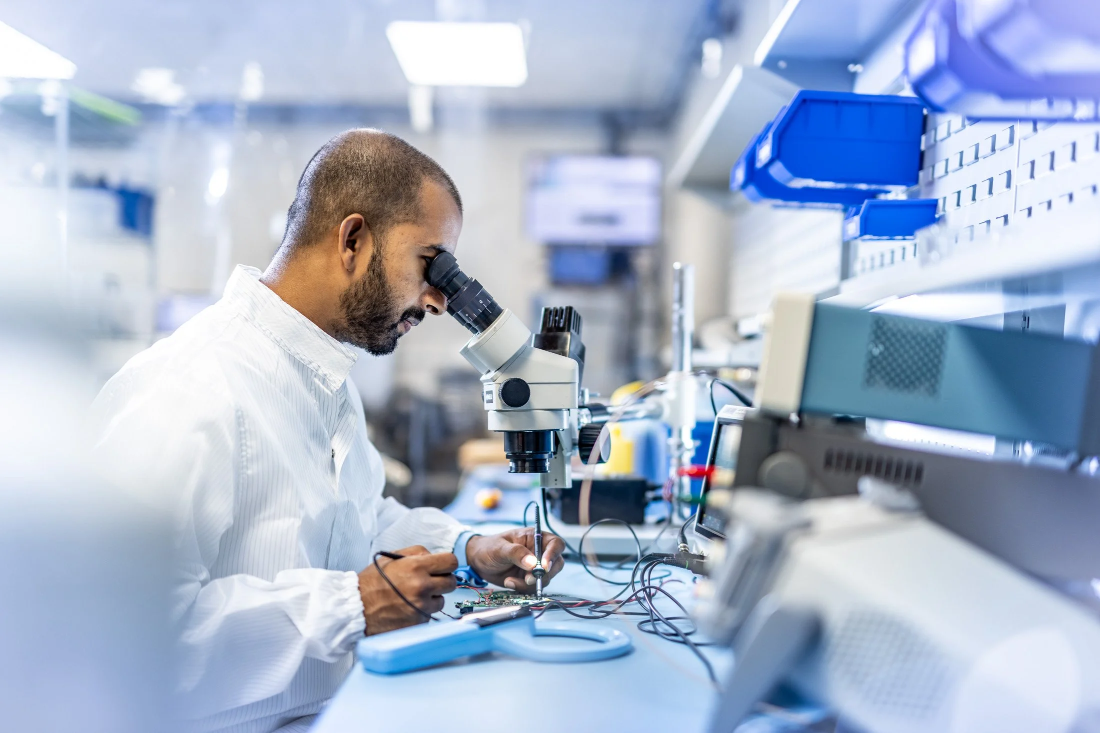 A scientist working in a laboratory, looking through a microscope while working on electronic components.