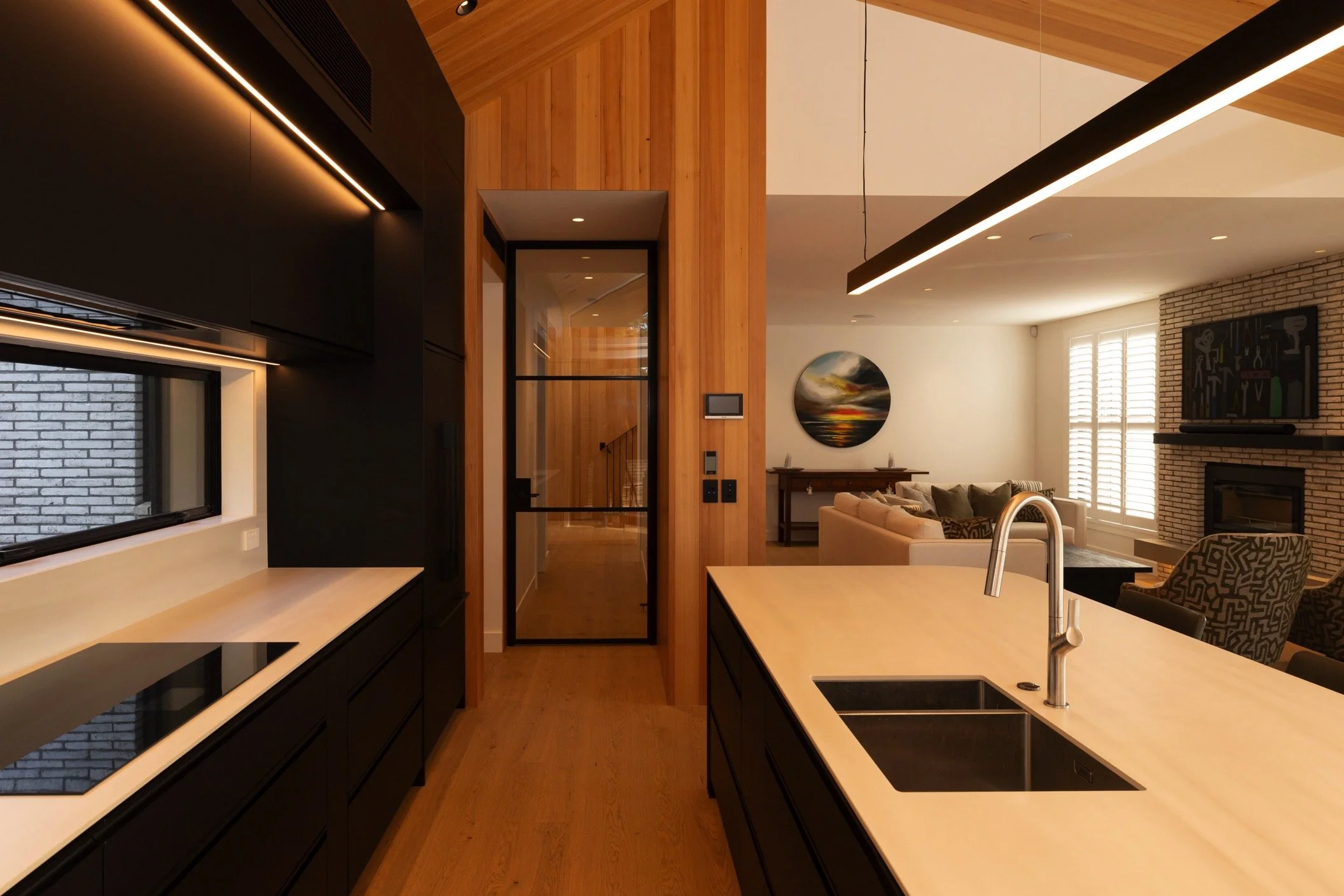 Modern open-plan kitchen and living area with sleek black cabinetry, light wood finishes, and minimalist design. Featuring high-end appliances, integrated lighting, and contemporary architectural elements, this stylish home interior showcases luxury