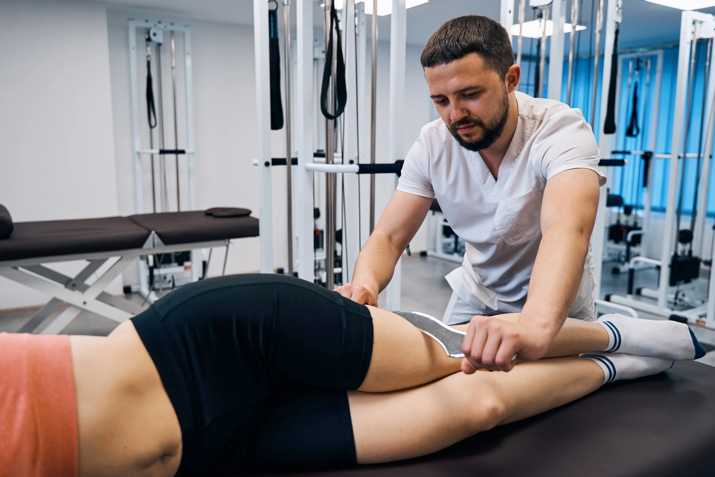 Physiotherapist massaging young woman with tool. Masseur treats sport injury with IASTM treatment