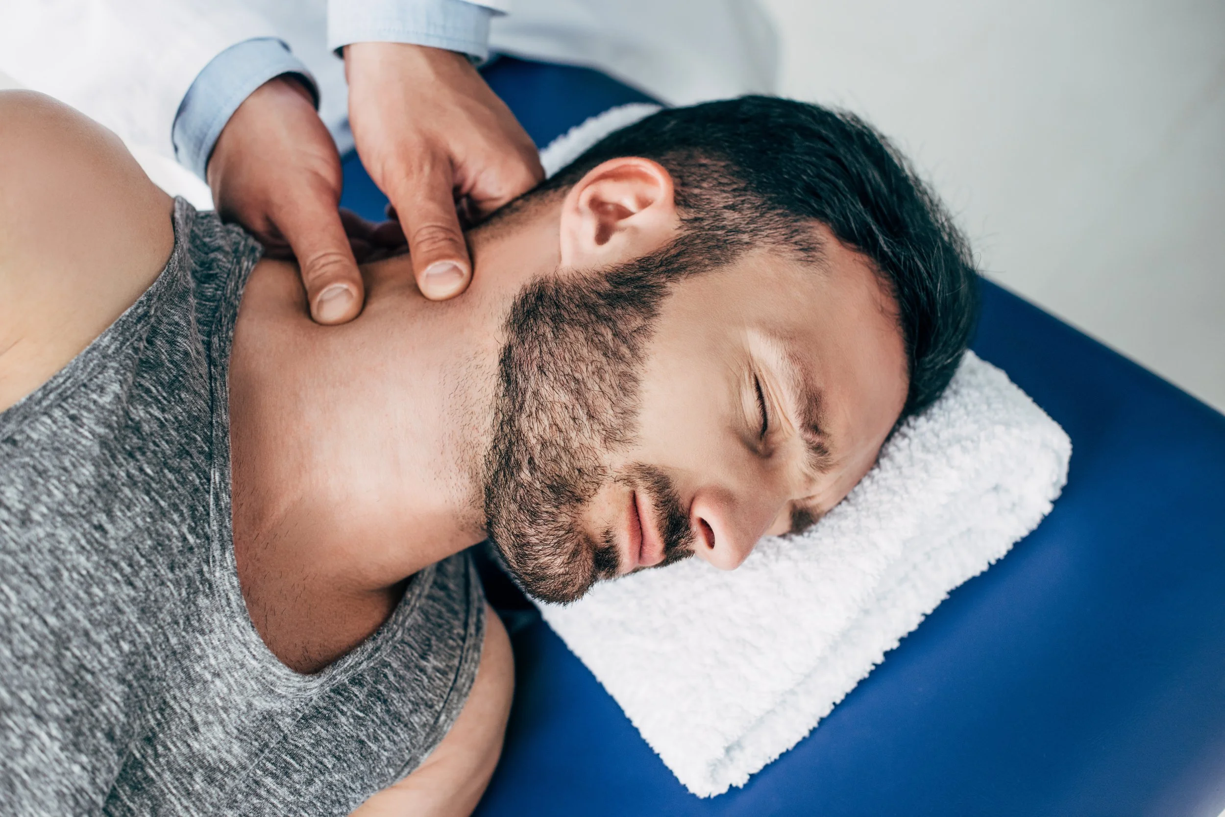 chiropractor massaging neck of man lying on Massage Table