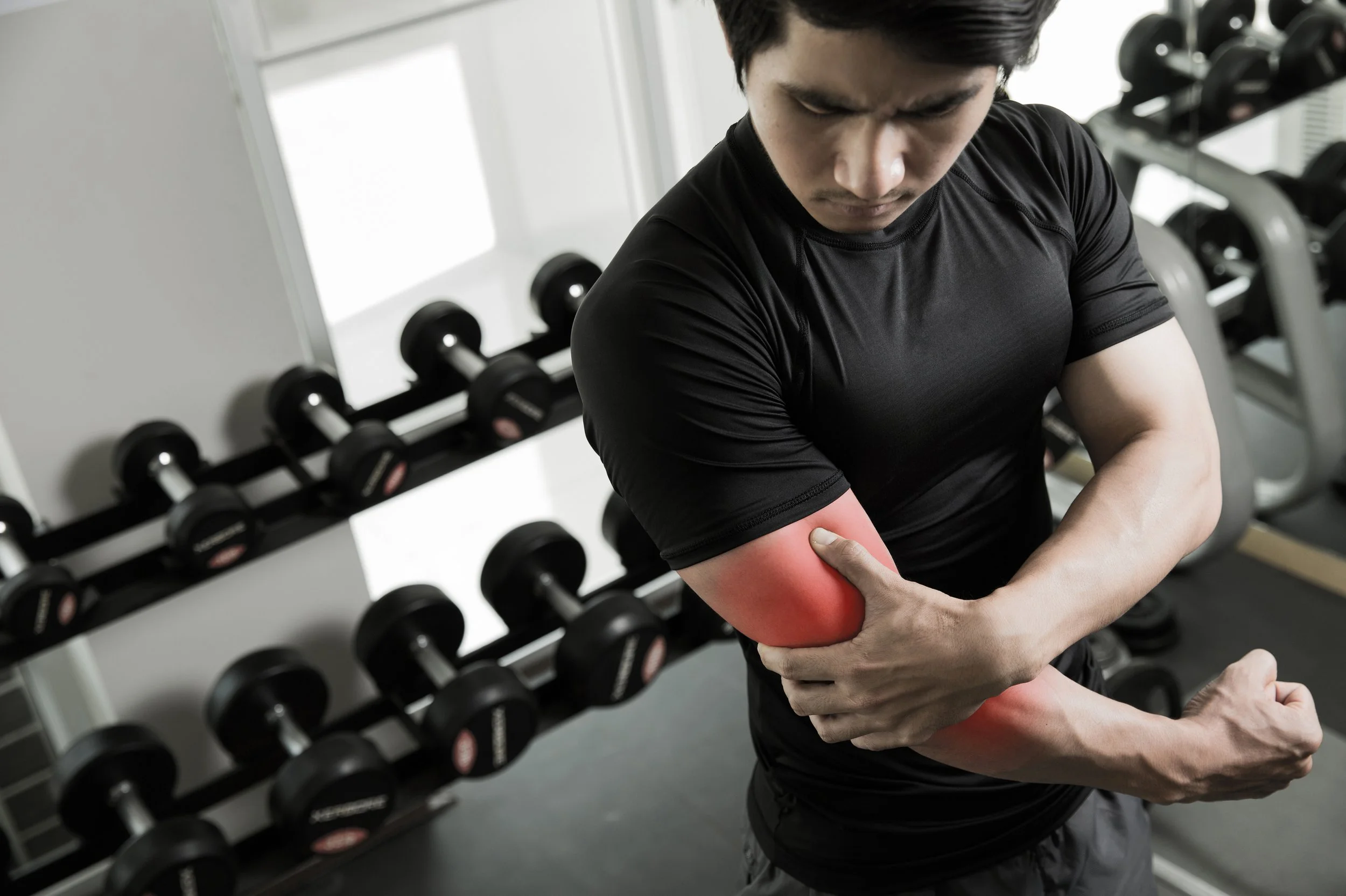 Man experiencing arm pain from weight lifting exercise in gym