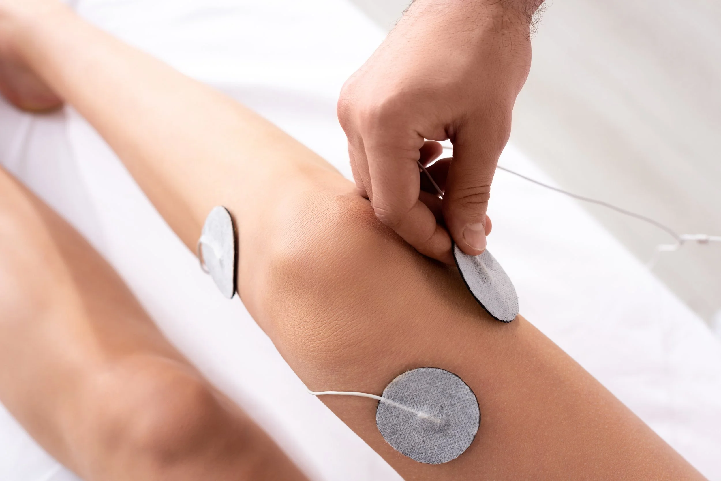 Top view of therapist setting electrodes on knee of patient with meniscus injury on massage couch