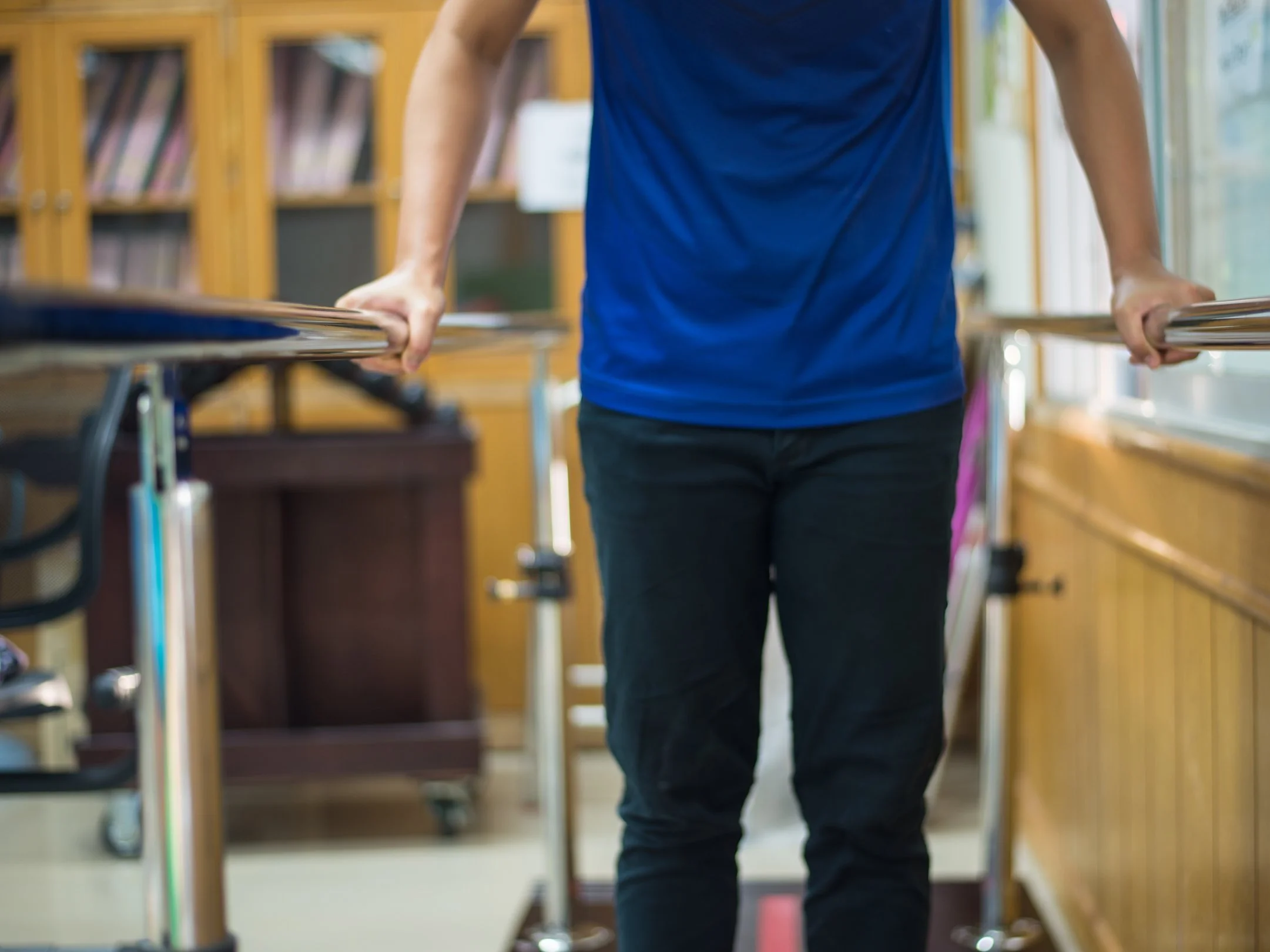 Person in blue shirt using parallel bars for rehabilitation