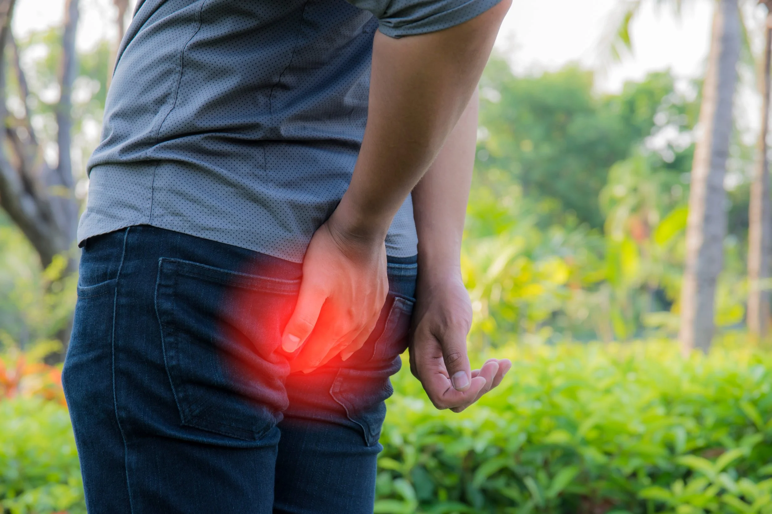 Person suffering from hemorrhoids with hand on affected area outdoors