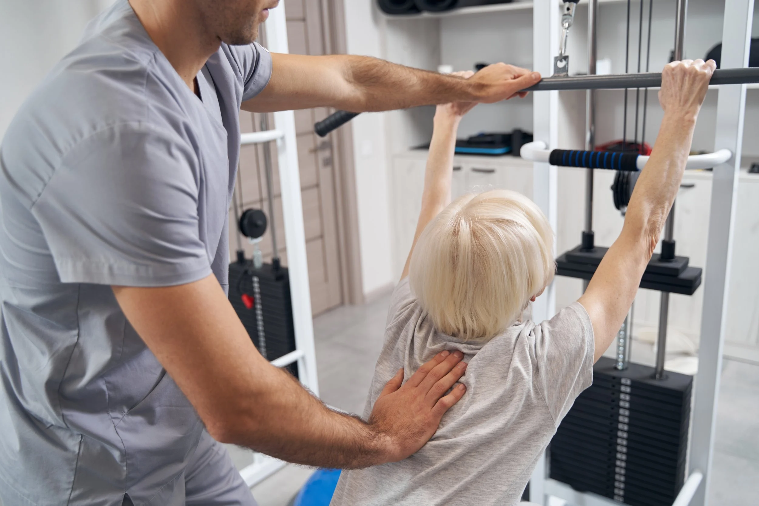 Manual therapist correcting old female posture during exercise