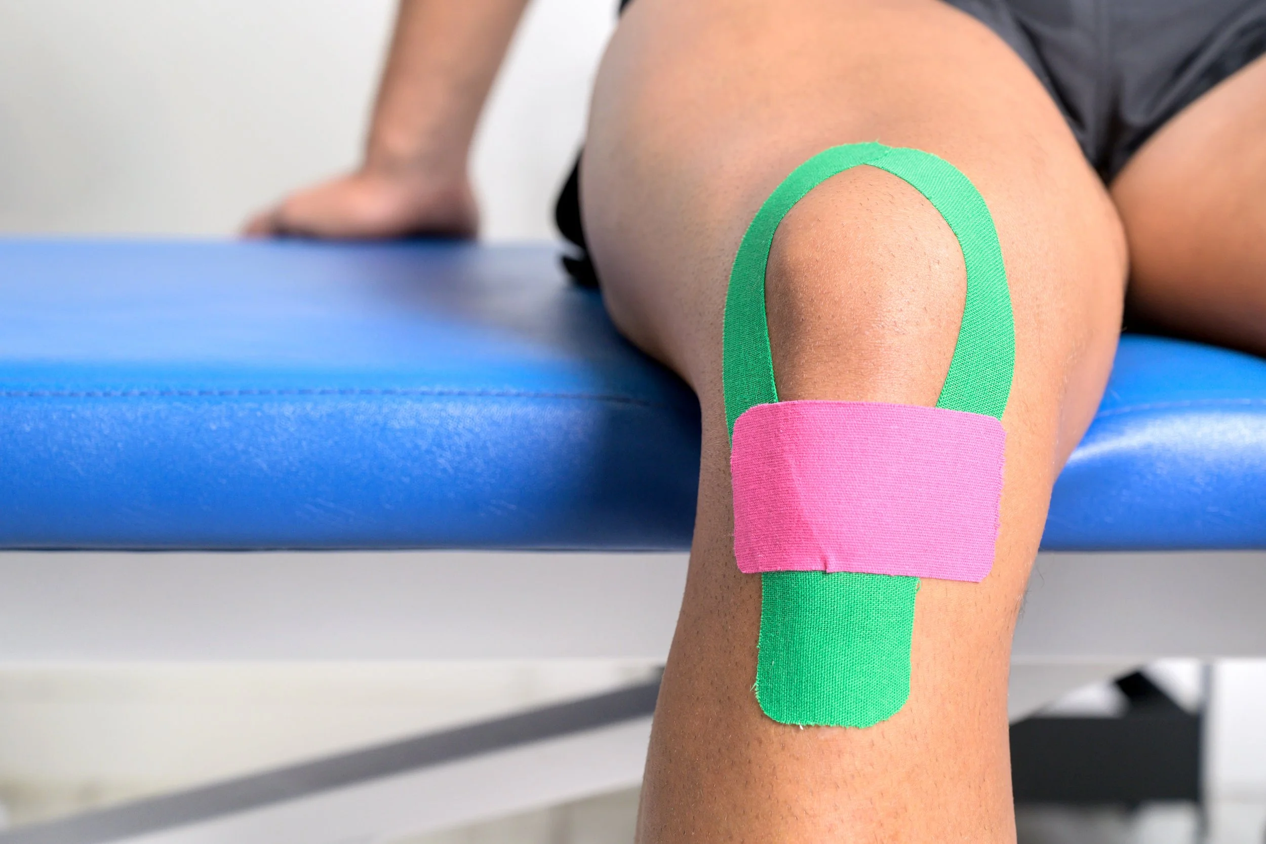 Young sportive male athlete treating injured knee with kinesio tape. Close up. Kinesiology, physical therapy, rehabilitation