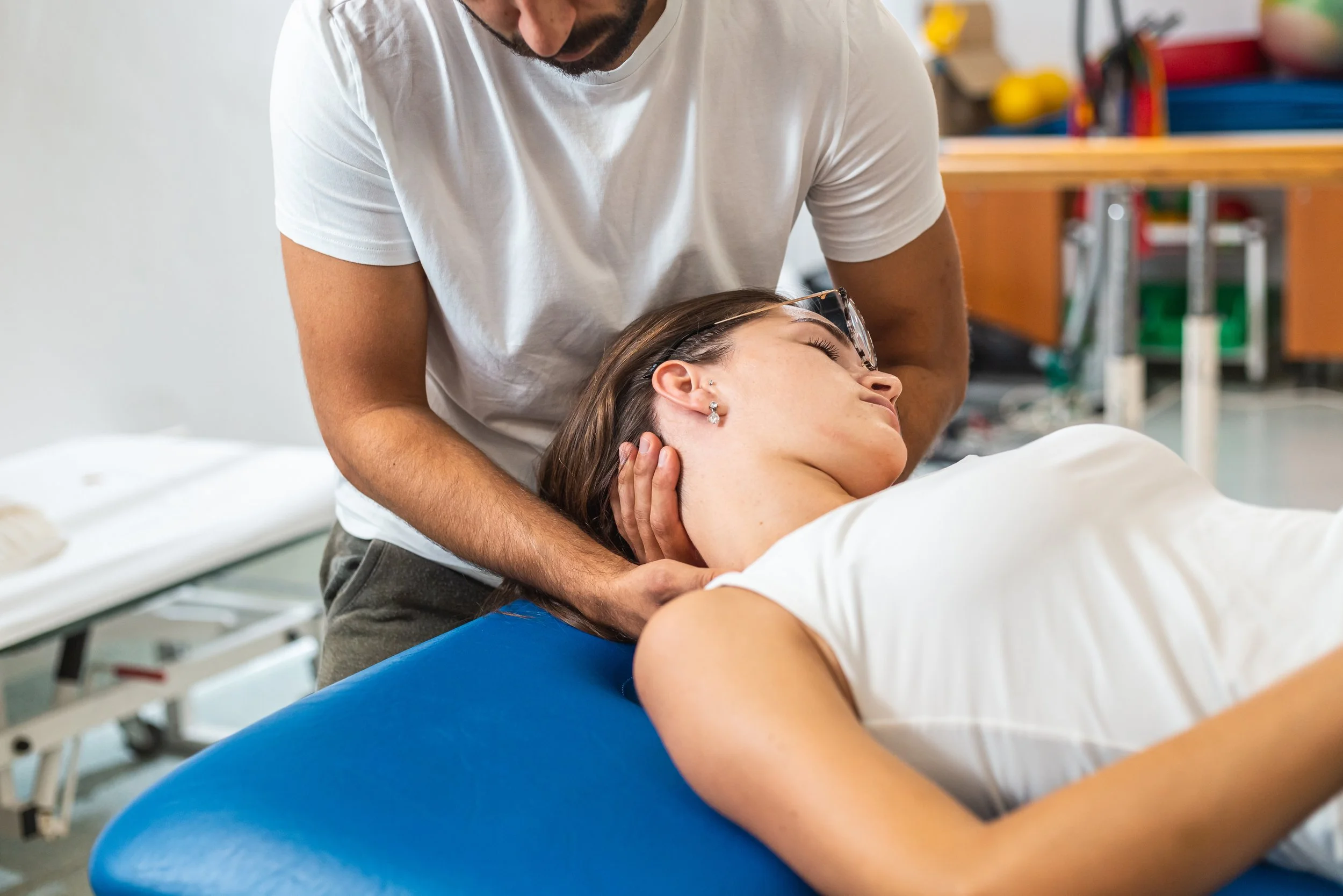 Close-up shot of a male physiotherapist doing manual neck stretching to a young Caucasian female patient.