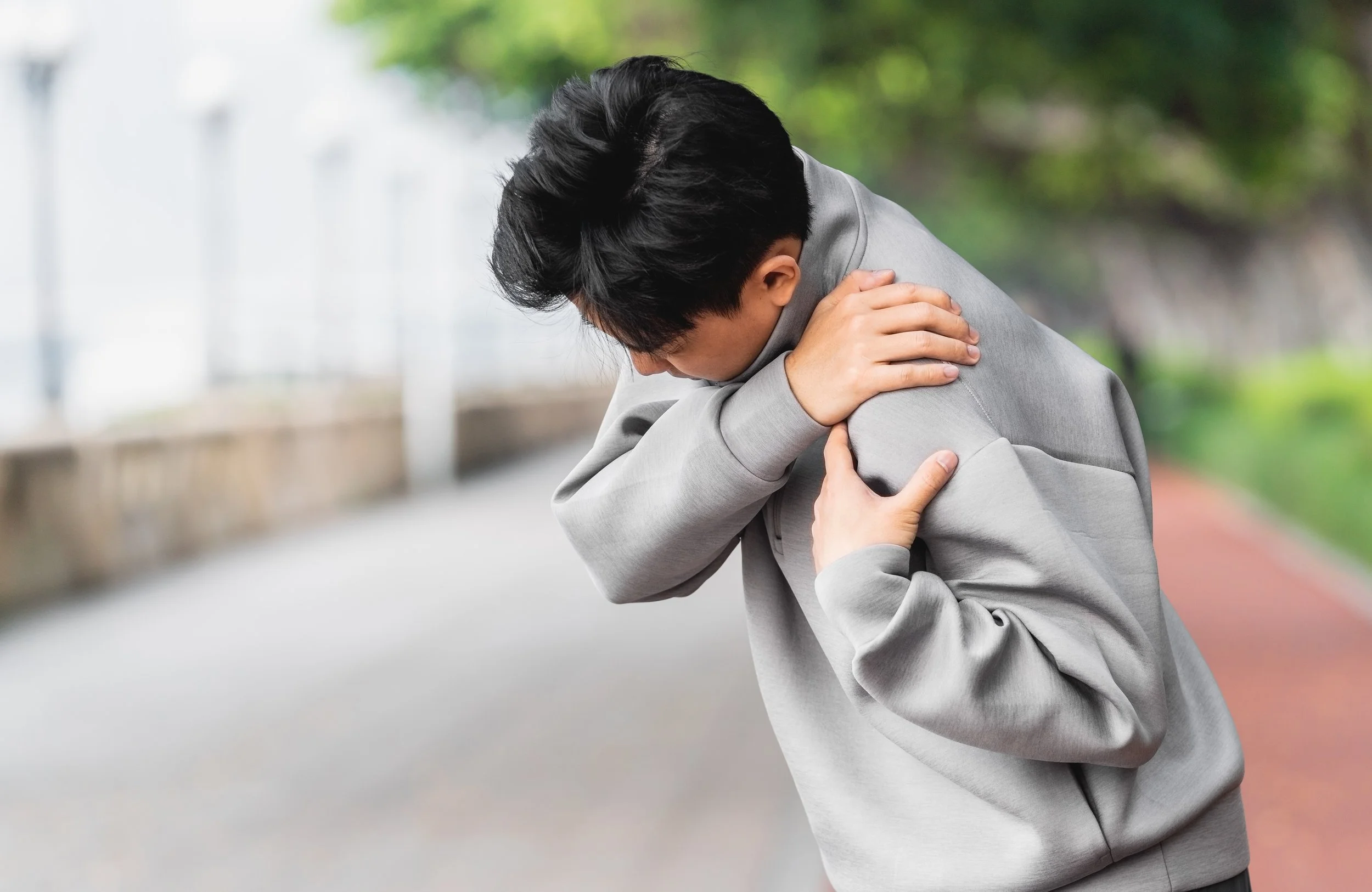 man is suffering from shoulder pain with hand covering on it
