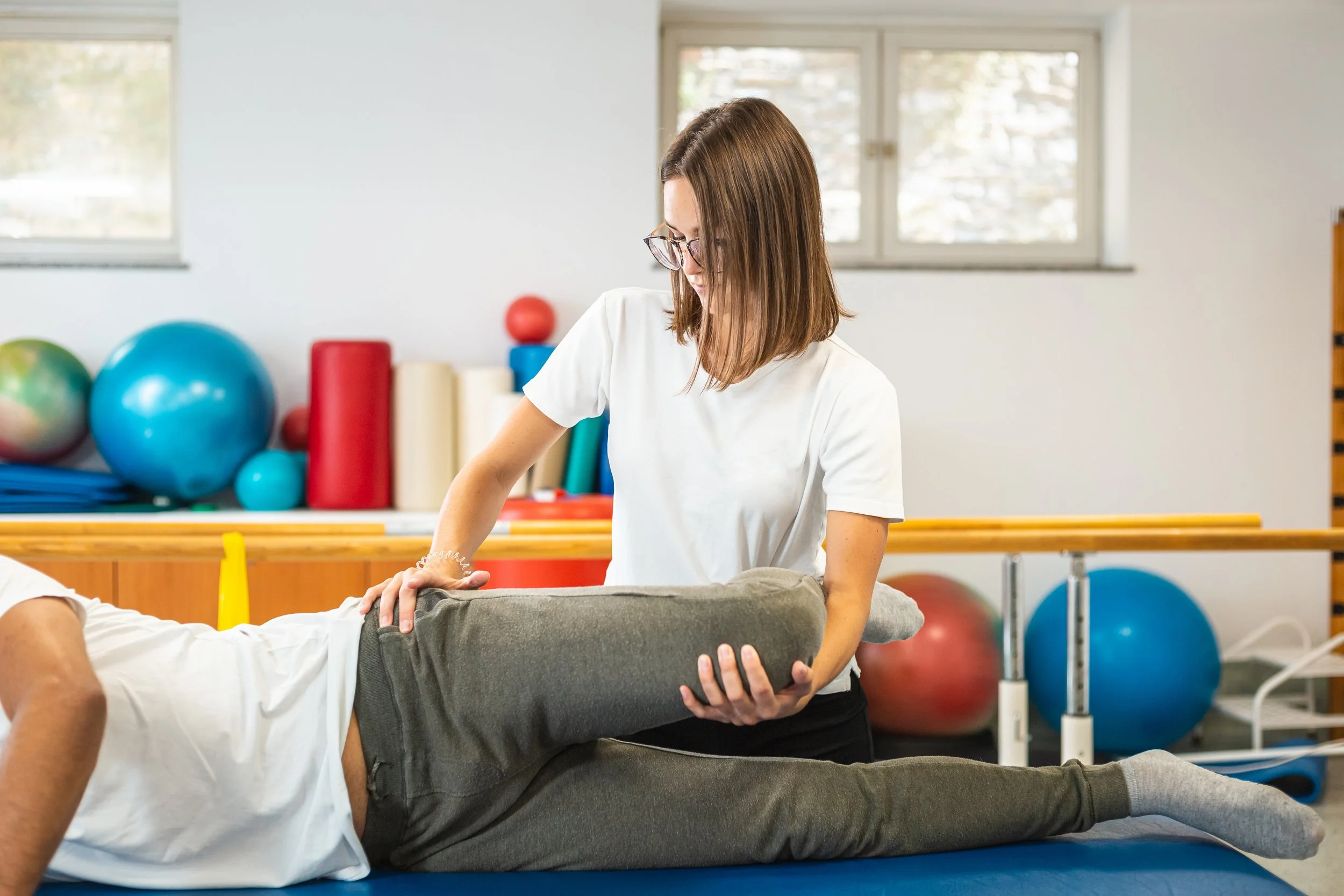 female physiotherapist doing leg and hip stretching treatment on a male patient for sciatica and radiating pain