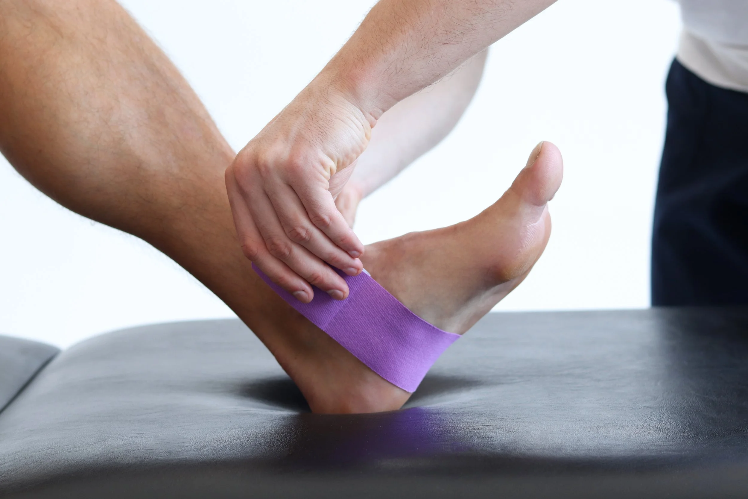 Kinesiology taping treatment with blue tape on male patient injured foot from achilles tendonitis. Sports injury kinesio treatment