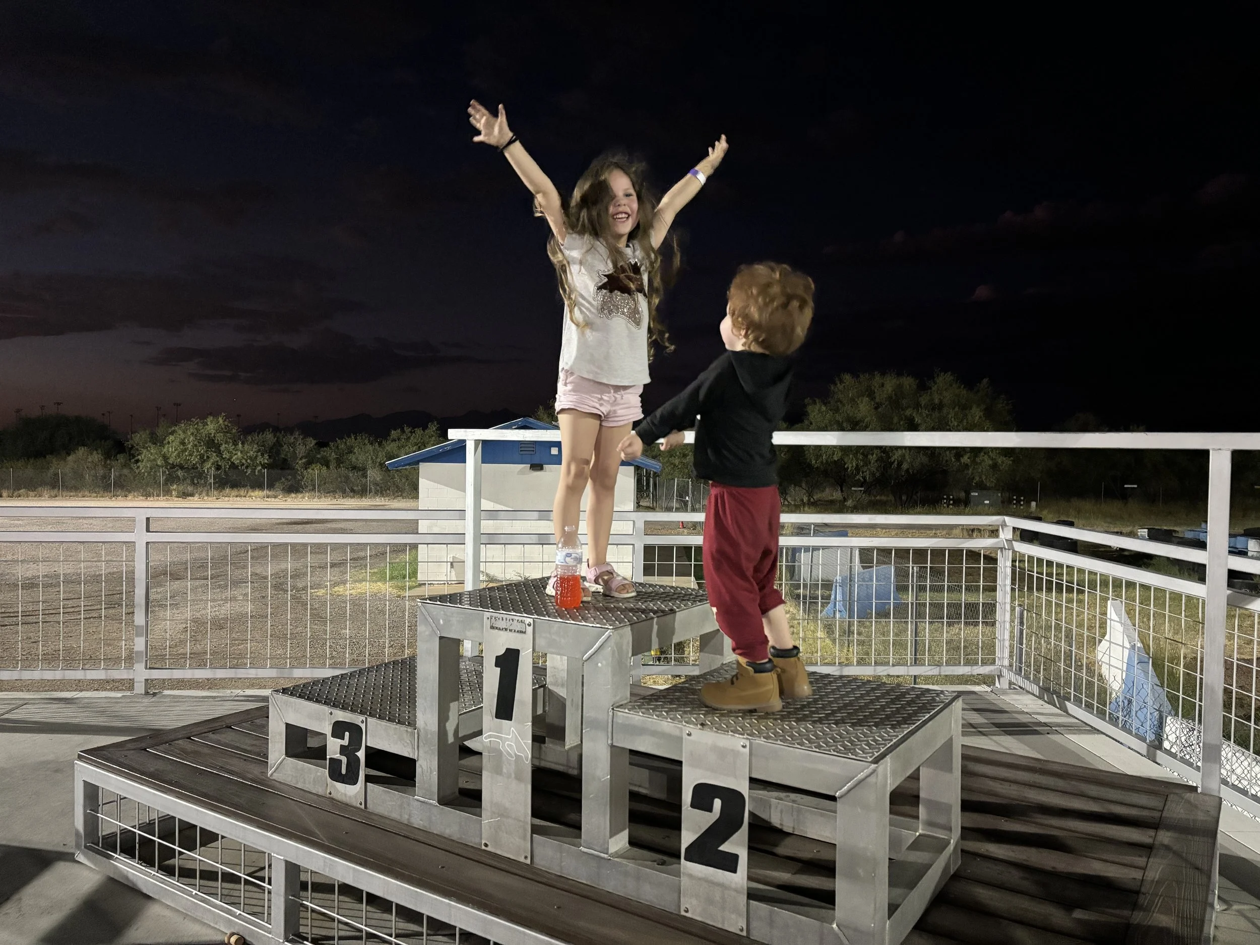 Two children on a podium with numbered platforms at night, one standing on the first place spot and the other on the second. Inspiration for the company Legends AZ.