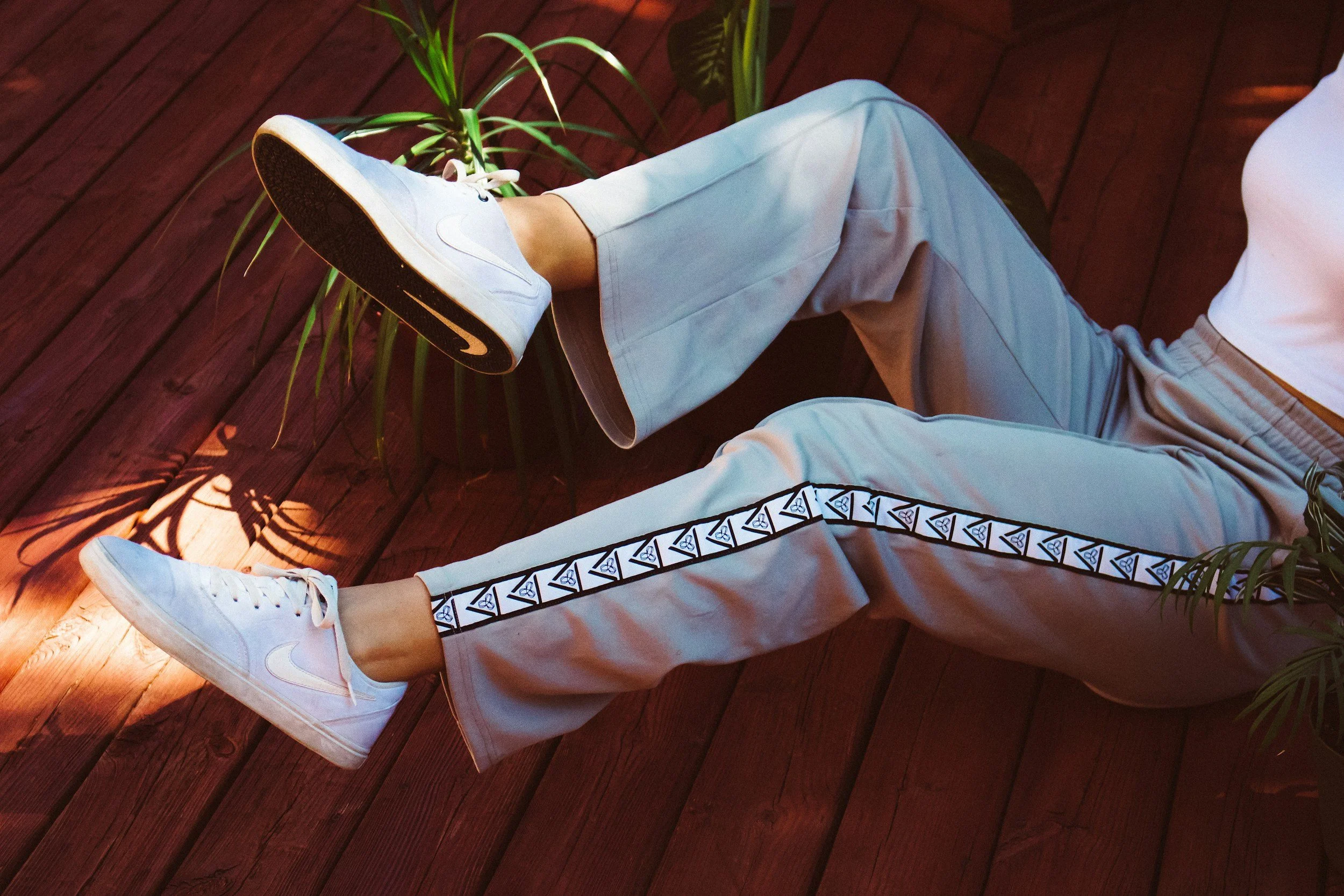 Person wearing light gray pants with geometric side stripe and white Nike sneakers, representing the Athleisure Collection on the Aglo Designs merchandise page.