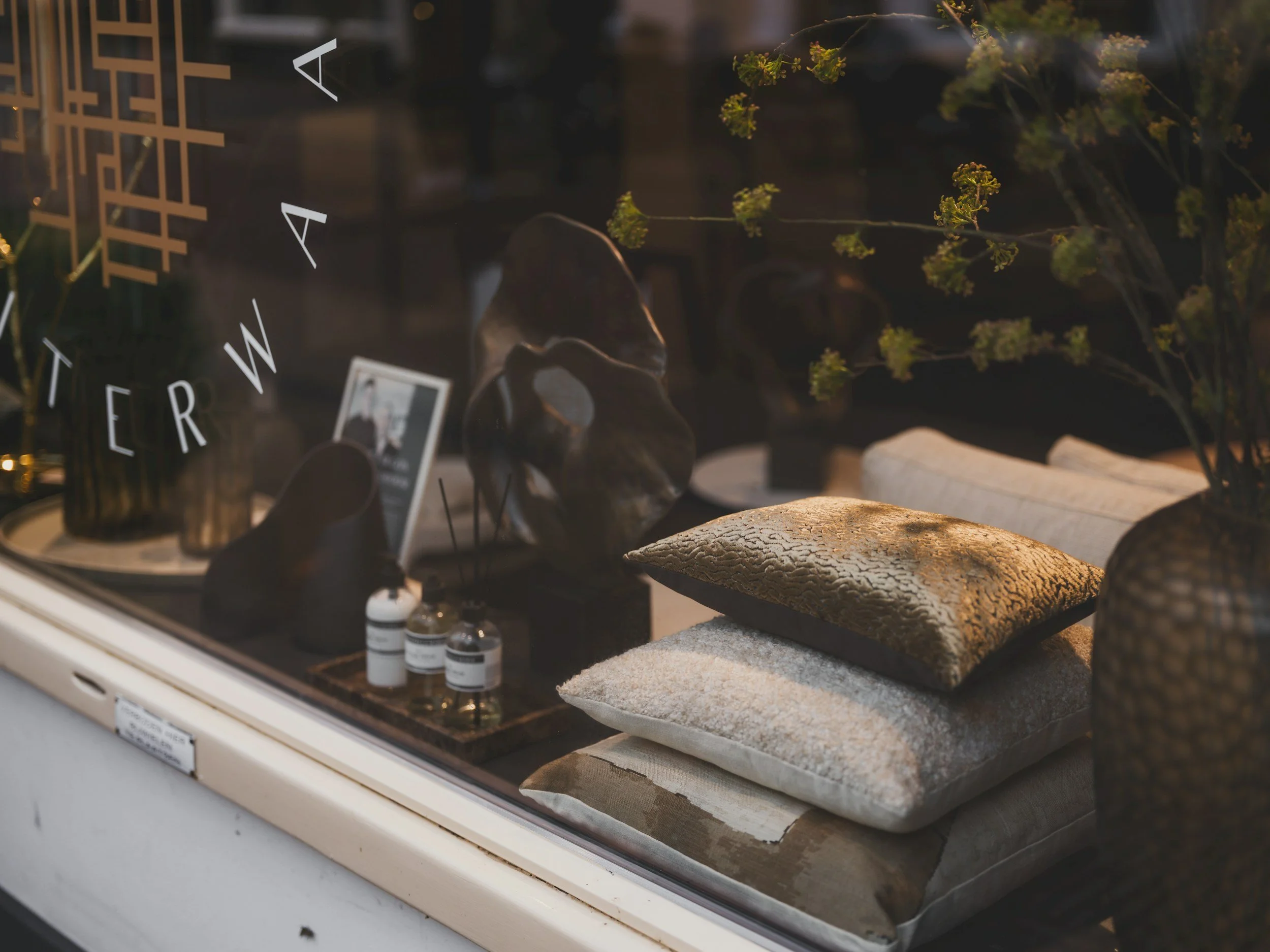 Storefront display with stacked cushions, sculptural accents, and decorative vases representing the Home Décor section on the Aglo Designs merchandise page.