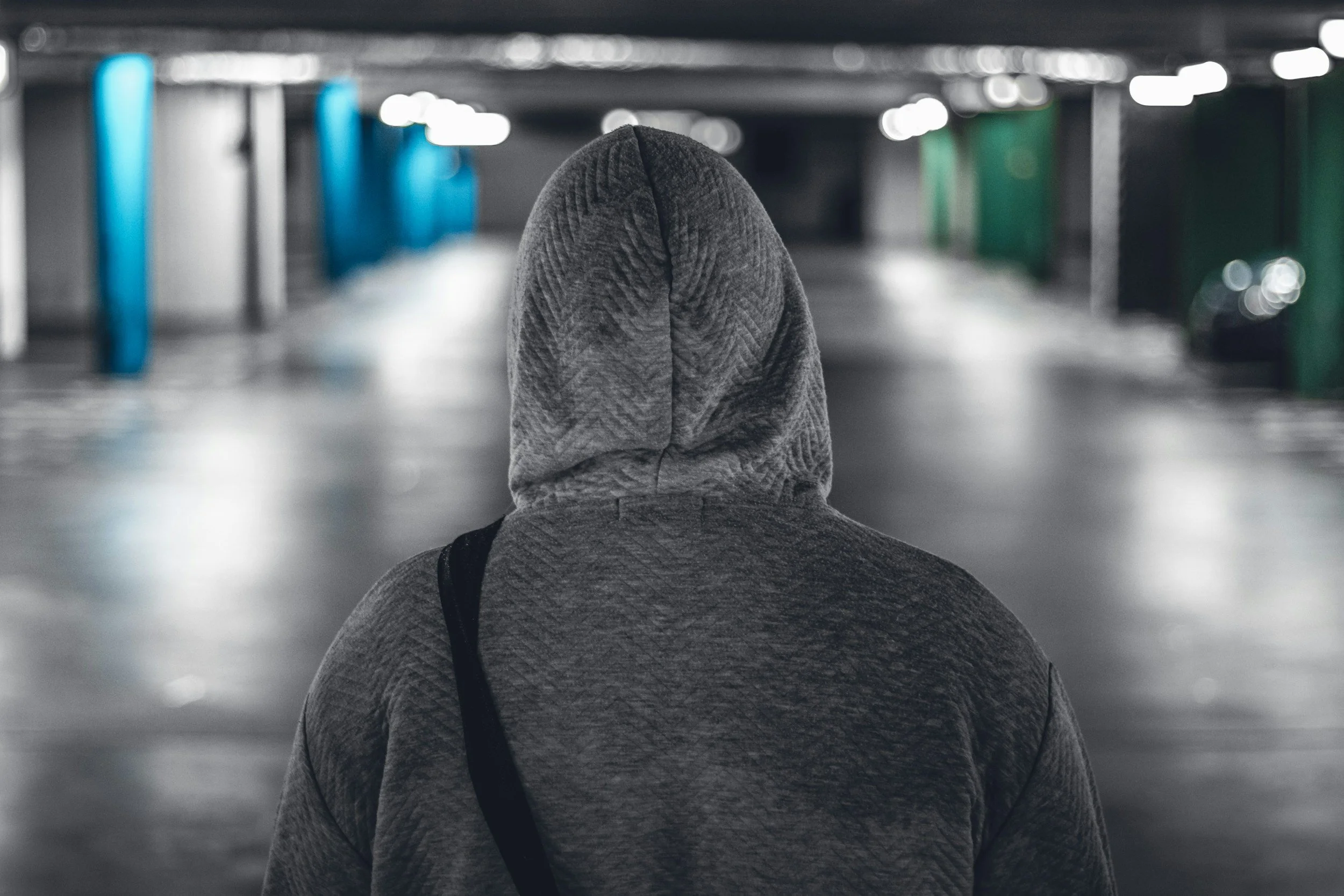 Back view of a person wearing a gray hoodie in an underground parking garage, representing the Men’s Outerwear section on the Aglo Designs merchandise page.
