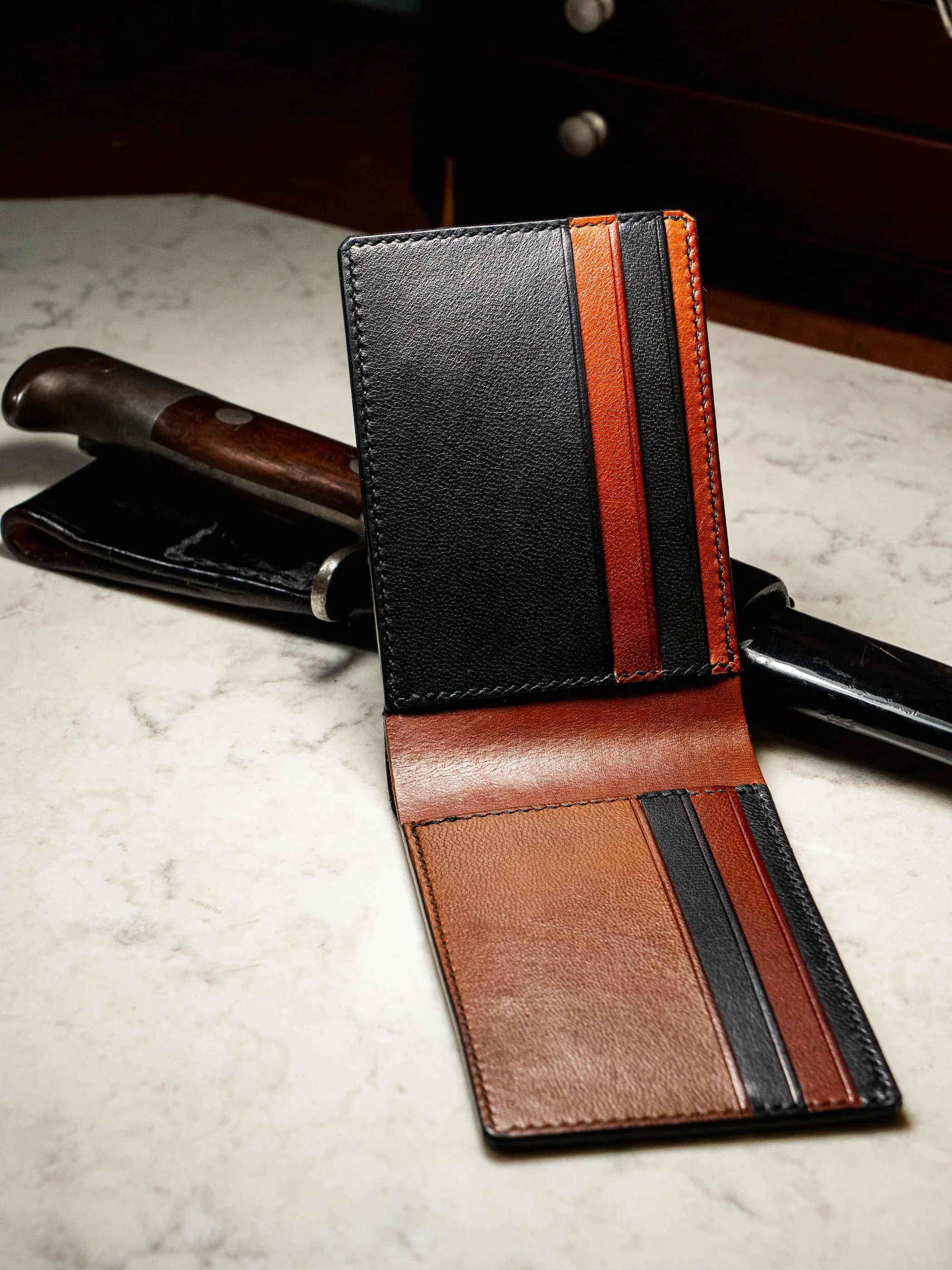 Open leather wallet with multiple card slots placed on a white marble surface, with a knife partially visible behind it.