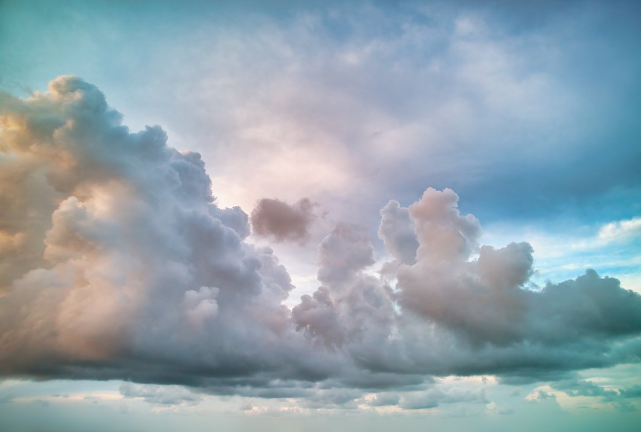 Cloudy sky with large, fluffy clouds and a hint of sunlight breaking through. Rumi, The guest house poem.